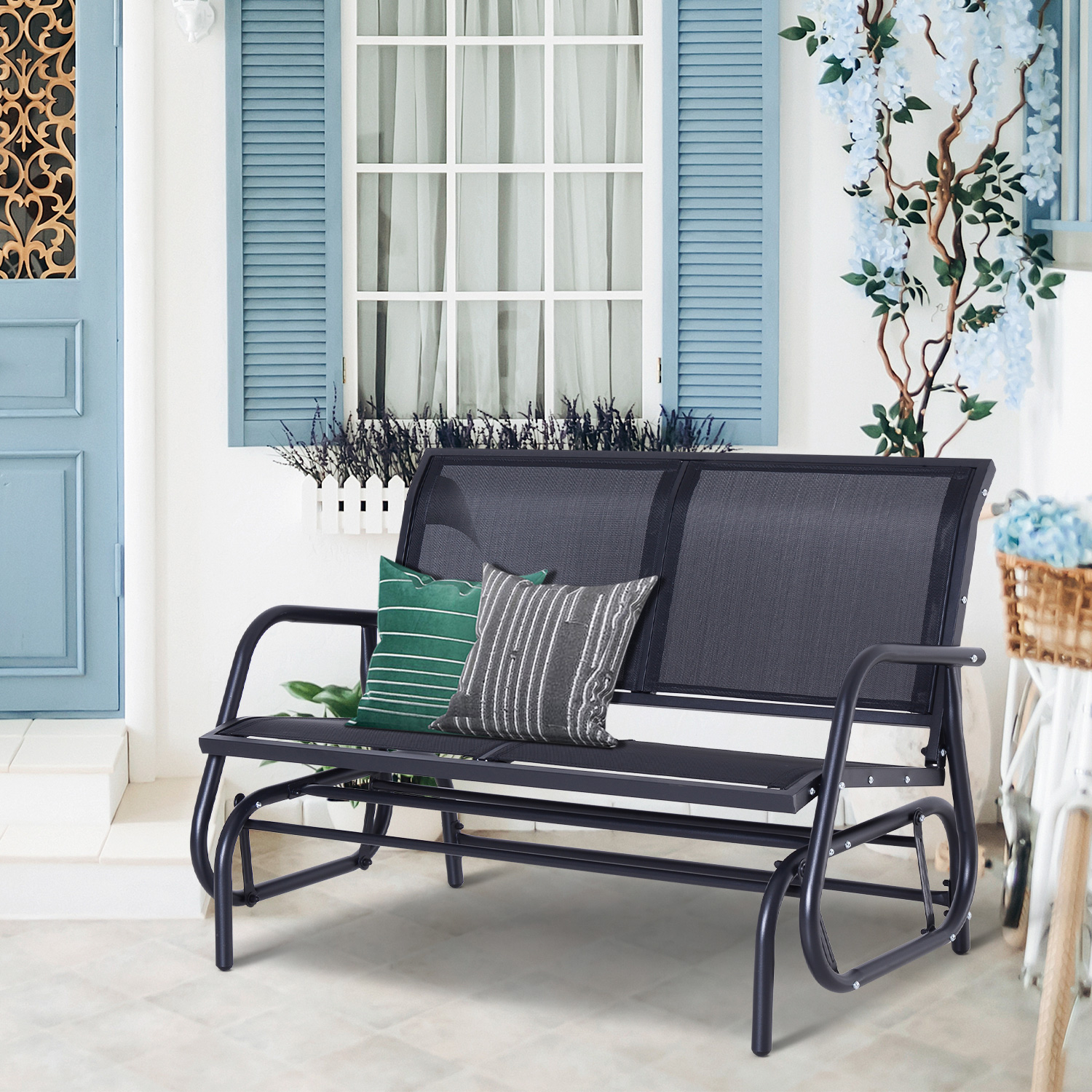 Eine schwarze Schaukelbank auf einer Veranda mit Kissen, Tür und Blumen.