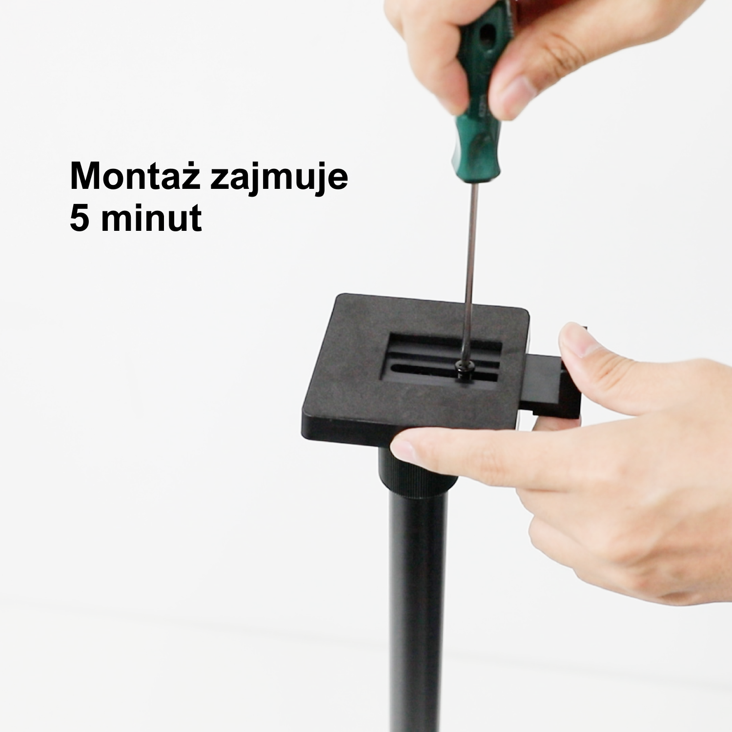 Osoba przykręca czarny stojak do podstawy śrubokrętem. Tło jest białe.