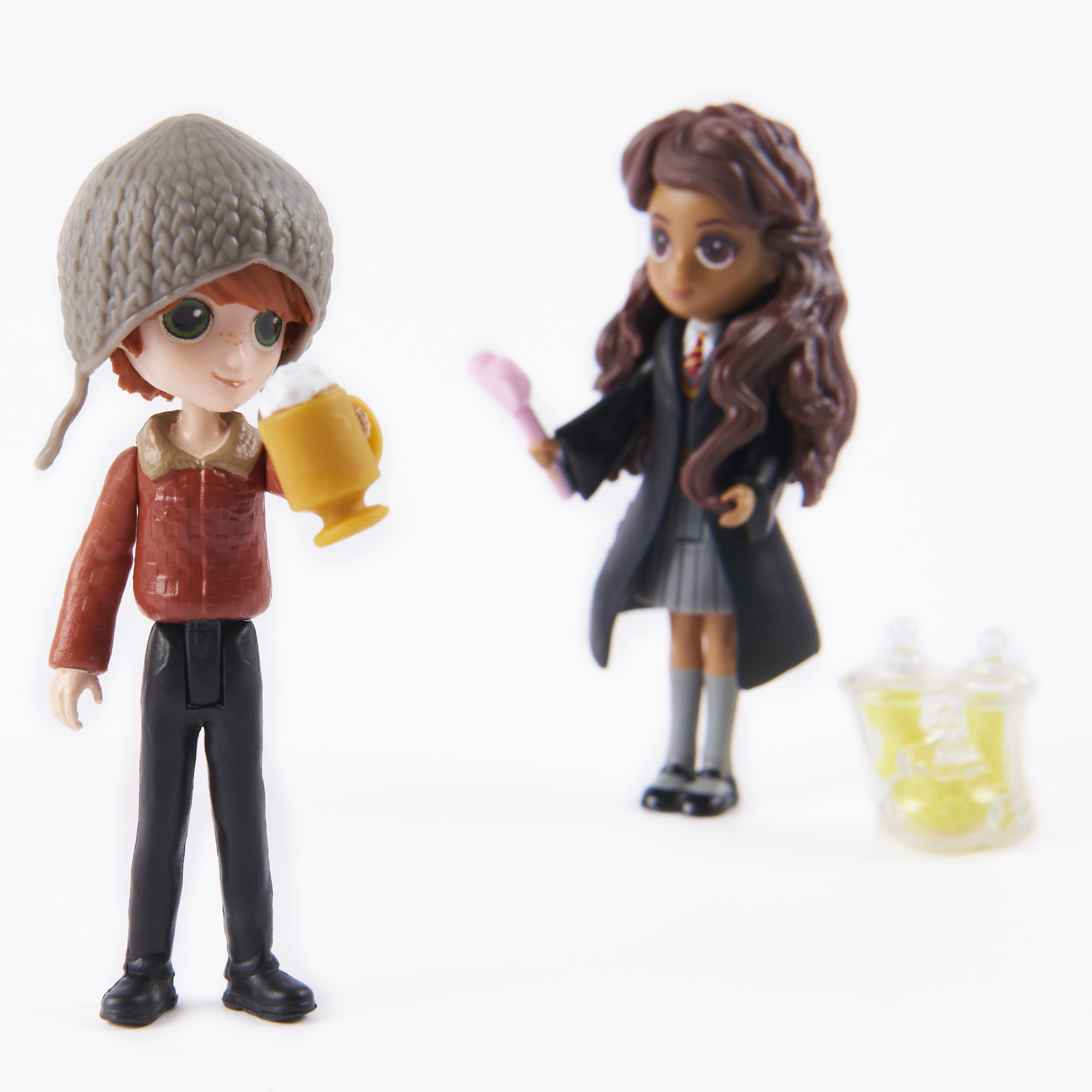 Figurine di Ron e Hermione, uno con una tazza, l'altro con una bacchetta e una fiala.