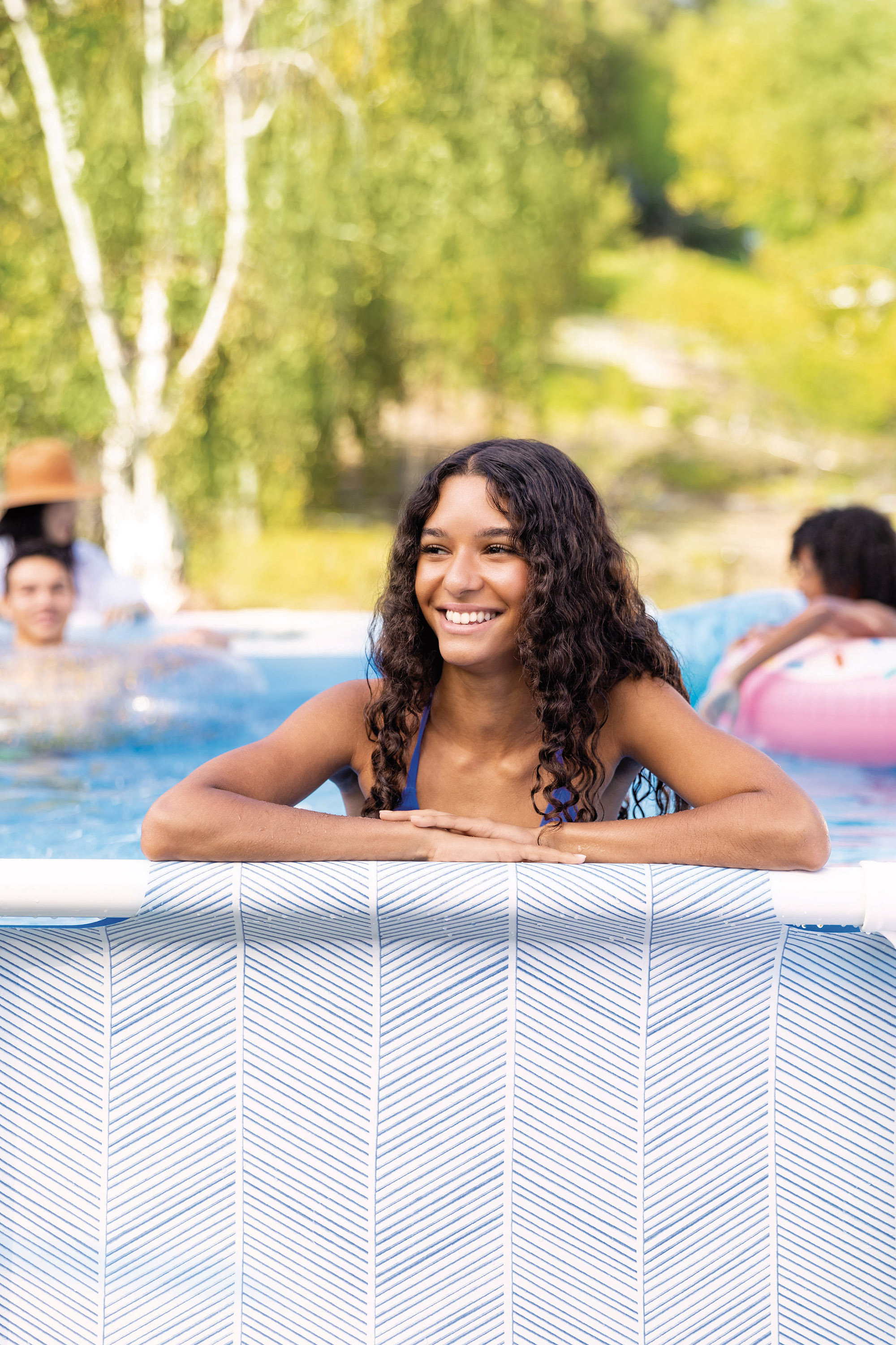 Frau lächelt in einem Pool, mit einer blau-weiß gemusterten Seite.