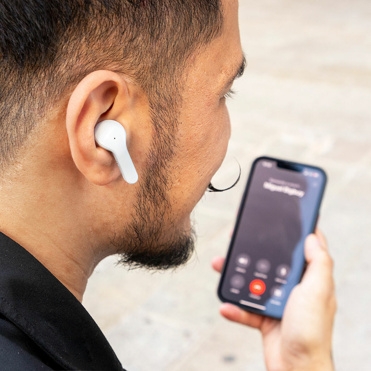 Ein Mann mit einem Ohrhörer im Ohr, der ein Telefon mit sichtbarem Anrufbildschirm hält.