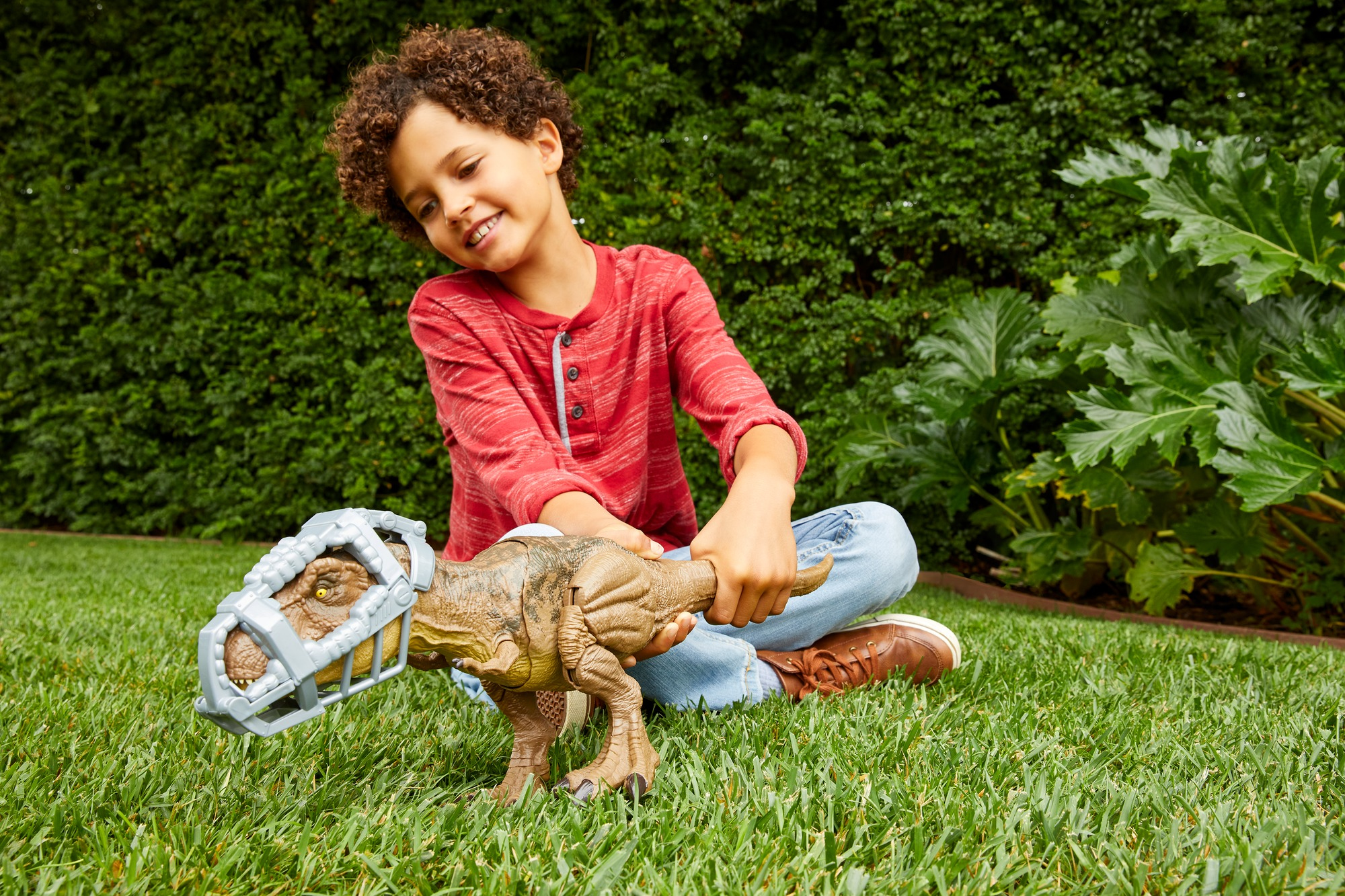 Niño jugando con un juguete de Tyrannosaurus Rex y una jaula. Hierba verde y arbustos.