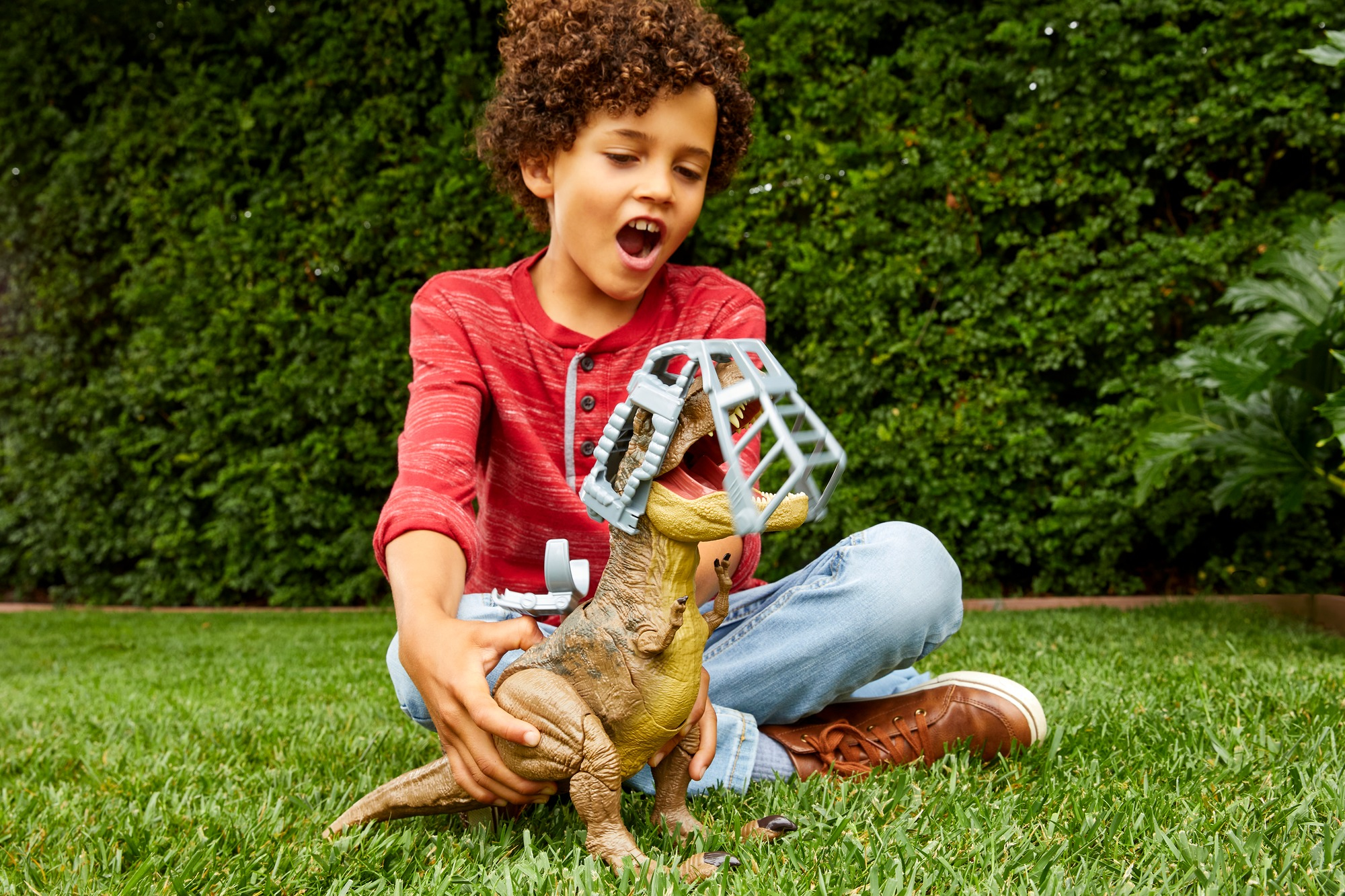 Niño jugando con un juguete de Tyrannosaurus Rex y jaula en un jardín. Hierba verde y arbustos.
