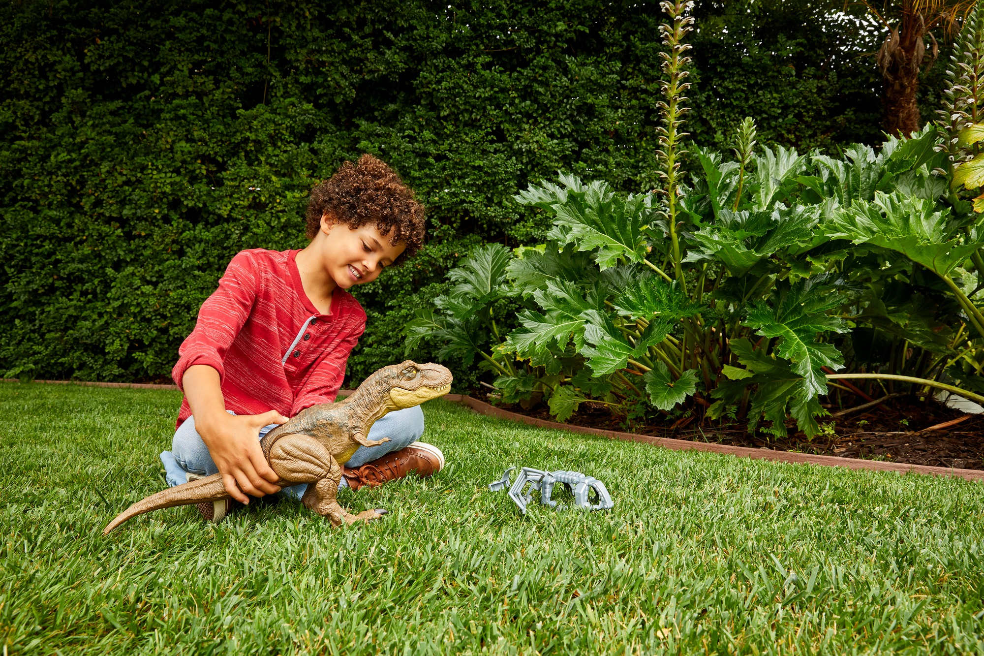 Un niño sosteniendo un dinosaurio de juguete sobre hierba, con un vehículo de juguete.
