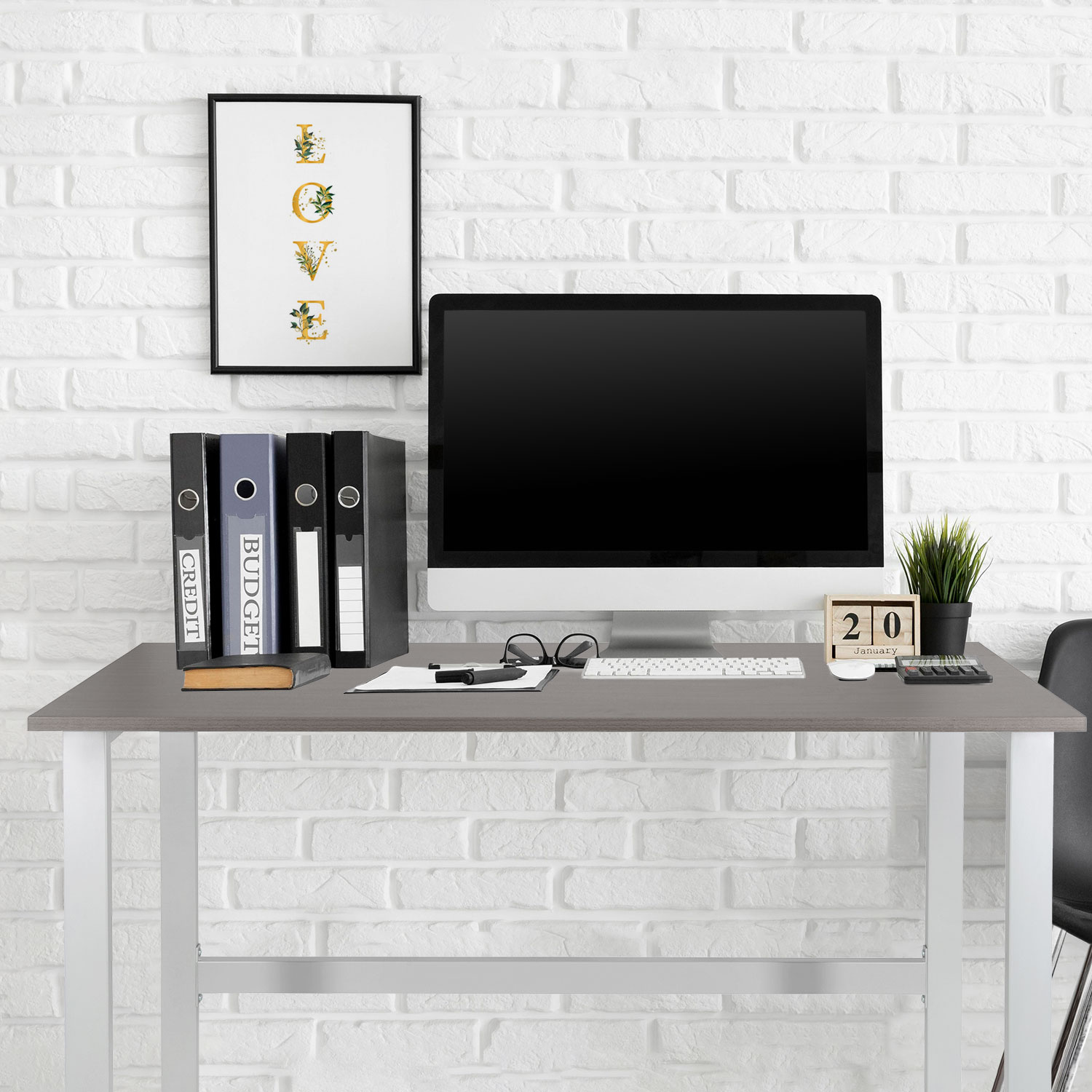 Schreibtisch mit Computer, Ordnern und einem Kalender. Weißer Backstein-Hintergrund.