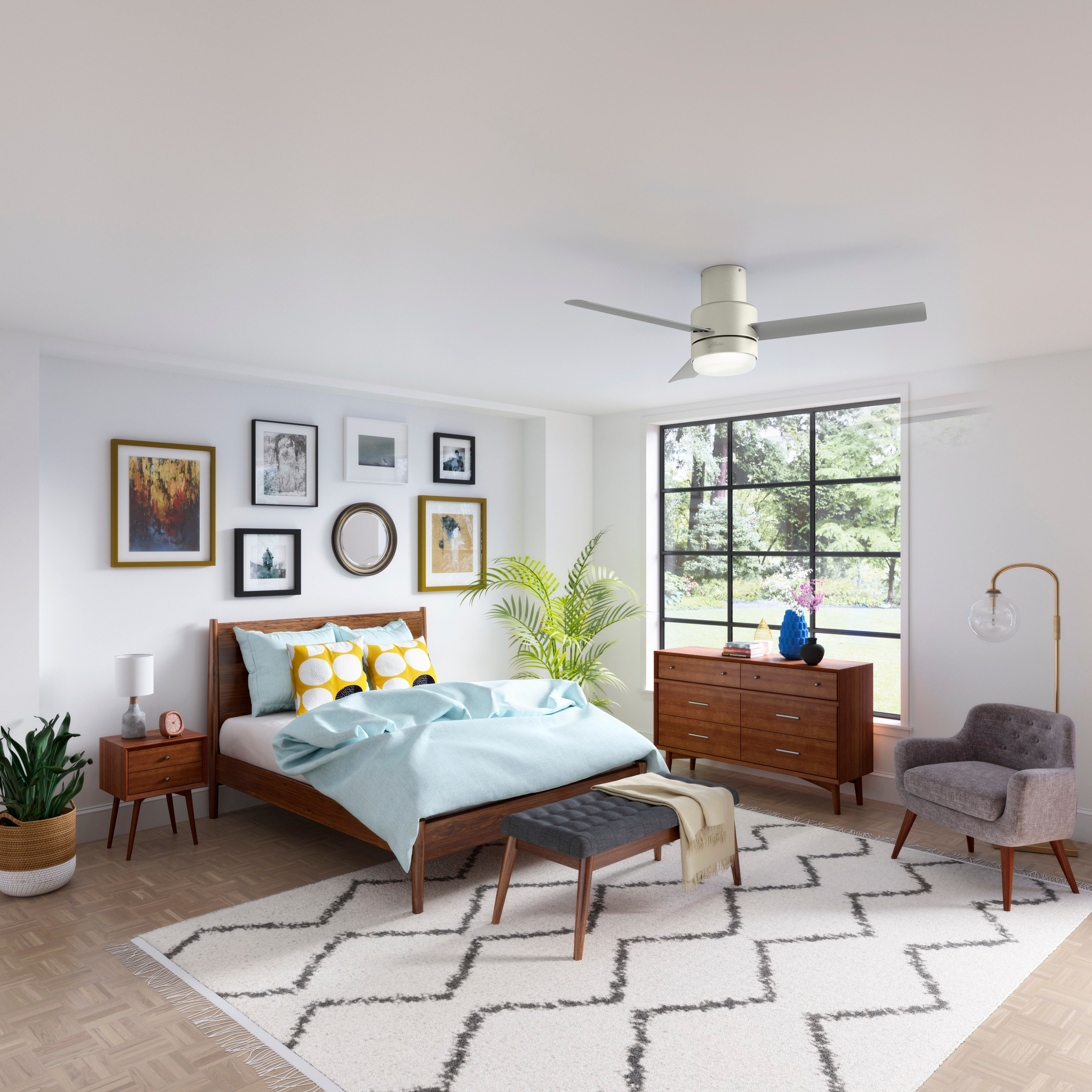 Ein Schlafzimmer mit Bett, Kommode und verschiedenen gerahmten Bildern. Ein Deckenventilator und ein Fenster sind sichtbar.