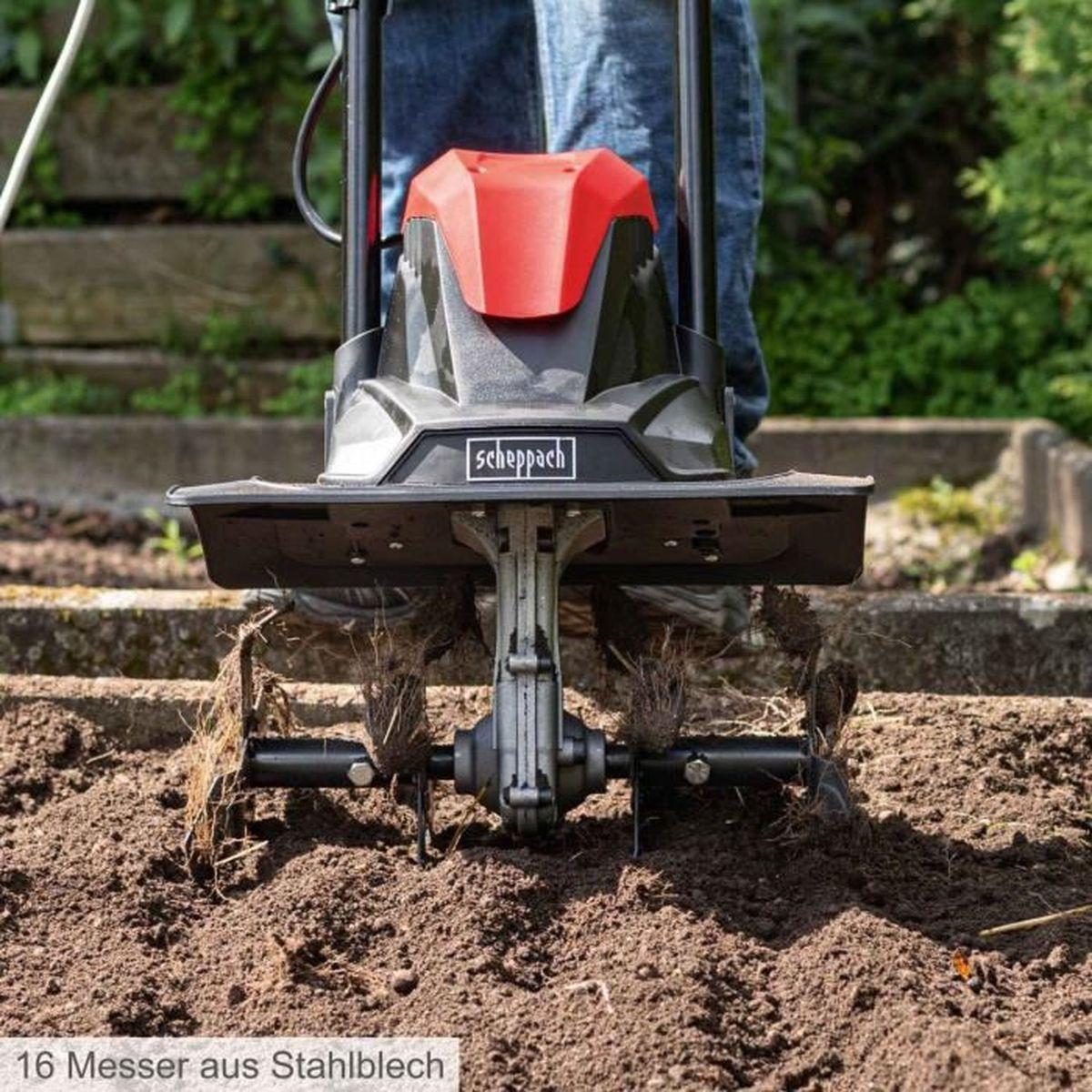 Primo piano del terreno lavorato da una motozappa rossa e nera. Sfondo di erba verde.
