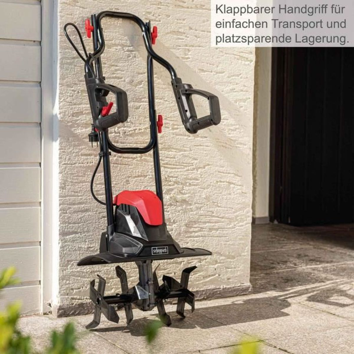 Una motozappa da giardino in piedi accanto a un muro bianco. Dettagli e maniglie rosse.