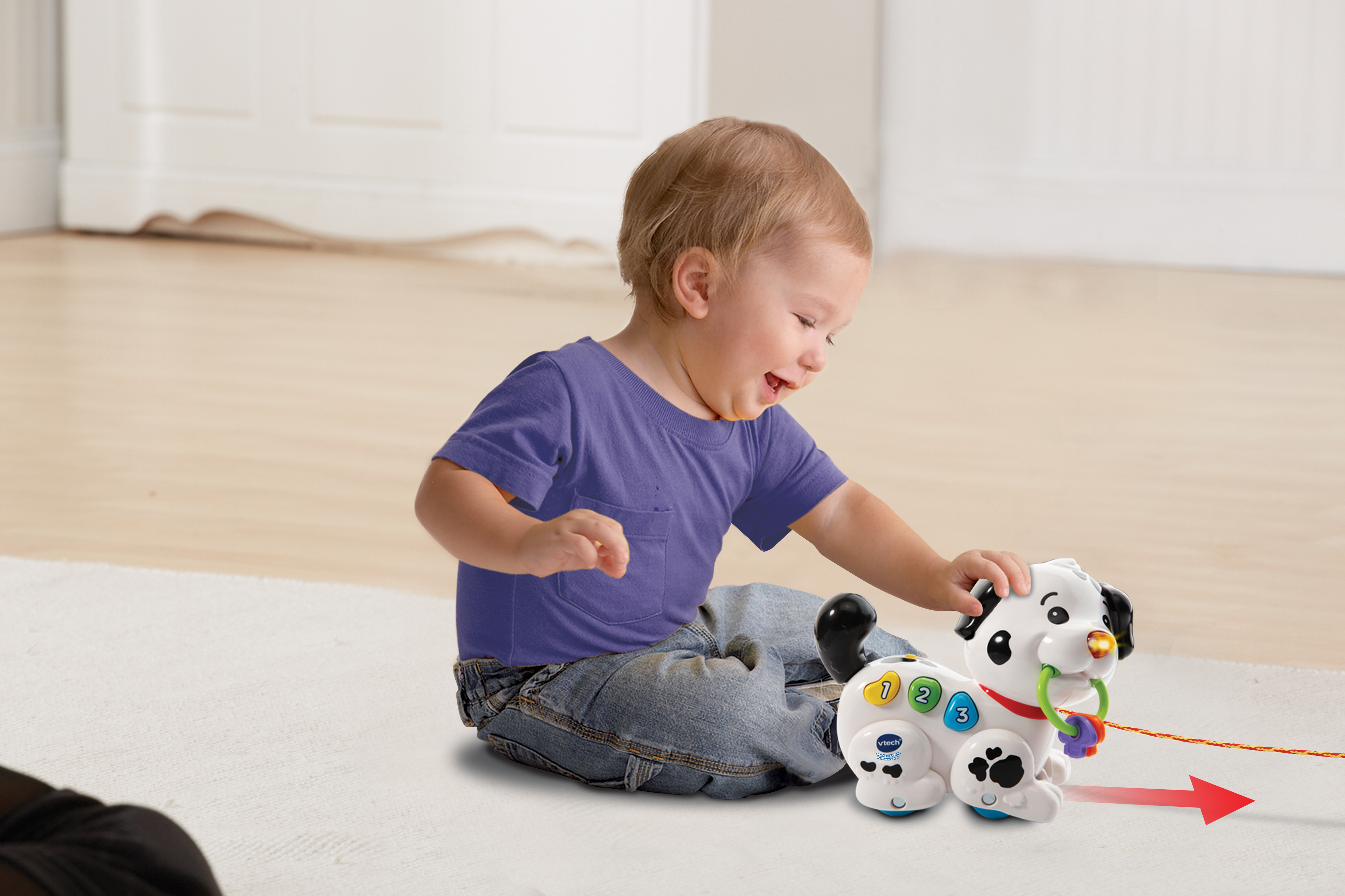 Małe dziecko bawi się zabawką w postaci psa. Zabawka ma numerowane przyciski. Sznur ciągnie się w prawo.