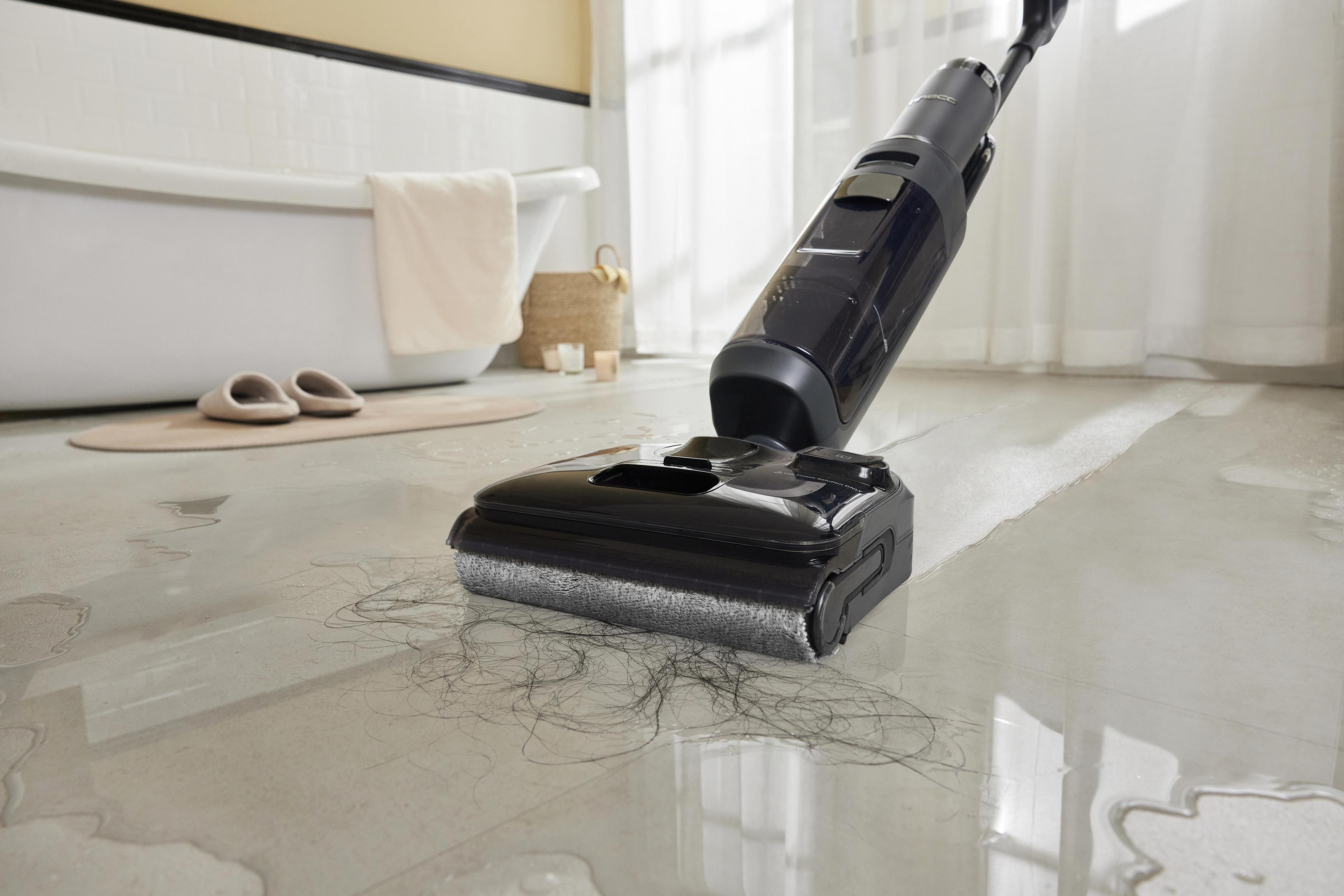 Czarny odkurzacz czyści mokrą, kafelkową podłogę. Tło pokazuje białą wannę i łazienkę.