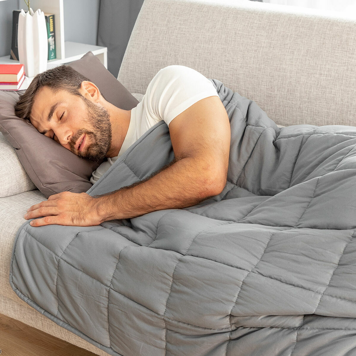 Uomo che dorme su un divano grigio sotto una coperta trapuntata grigia.