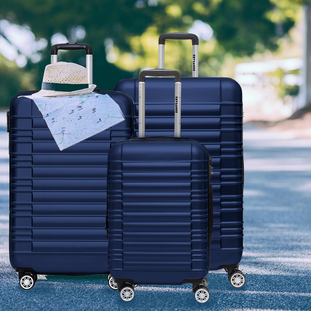 Three navy blue suitcases with handles and wheels, standing on a road with a hat.