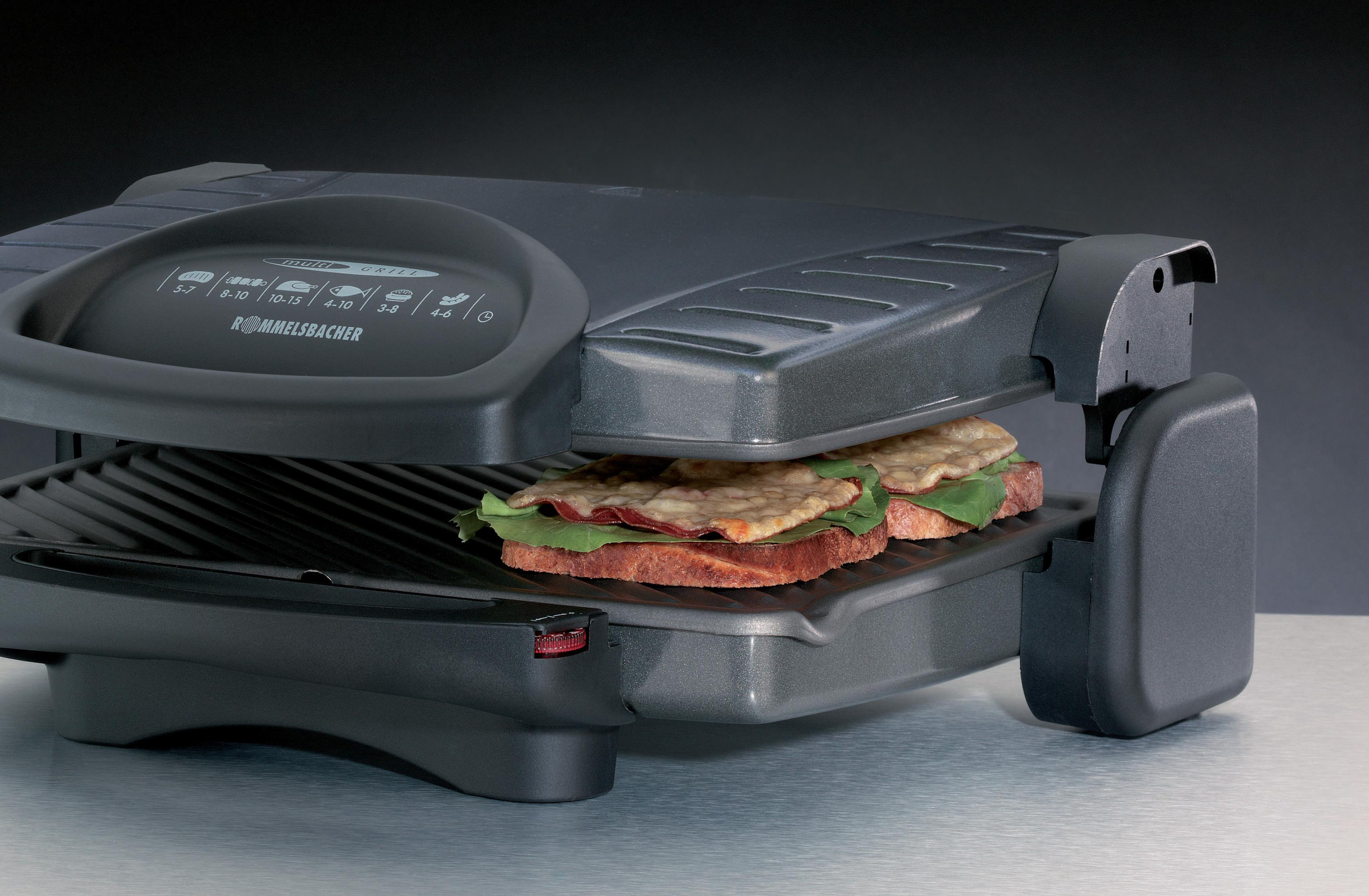 Grill do kanapek, otwarty, z dwoma kanapkami na dolnym ruszcie. Urządzenie jest szare z czarnym uchwytem.