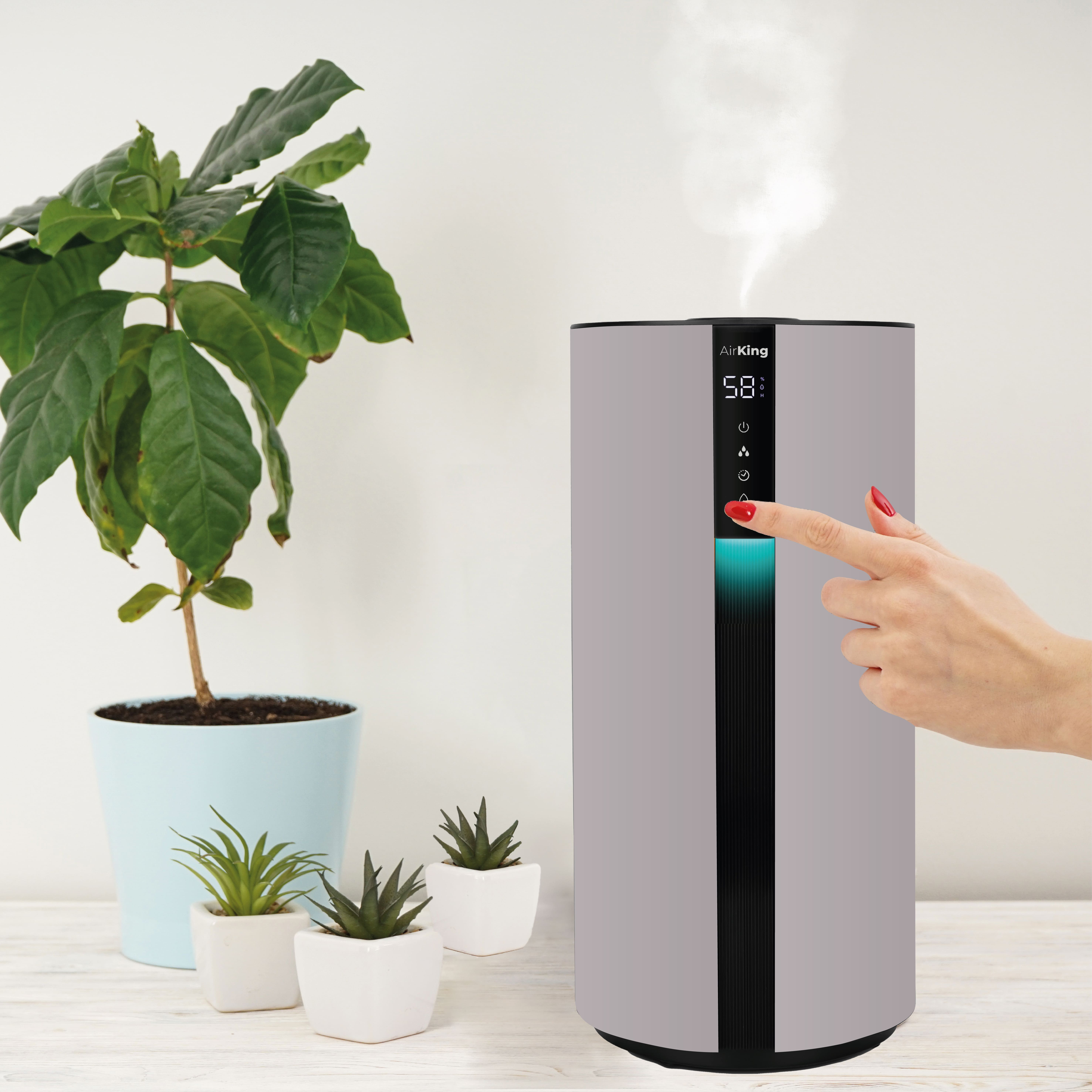A humidifier with digital display is being touched by a person. Plants are on the left.