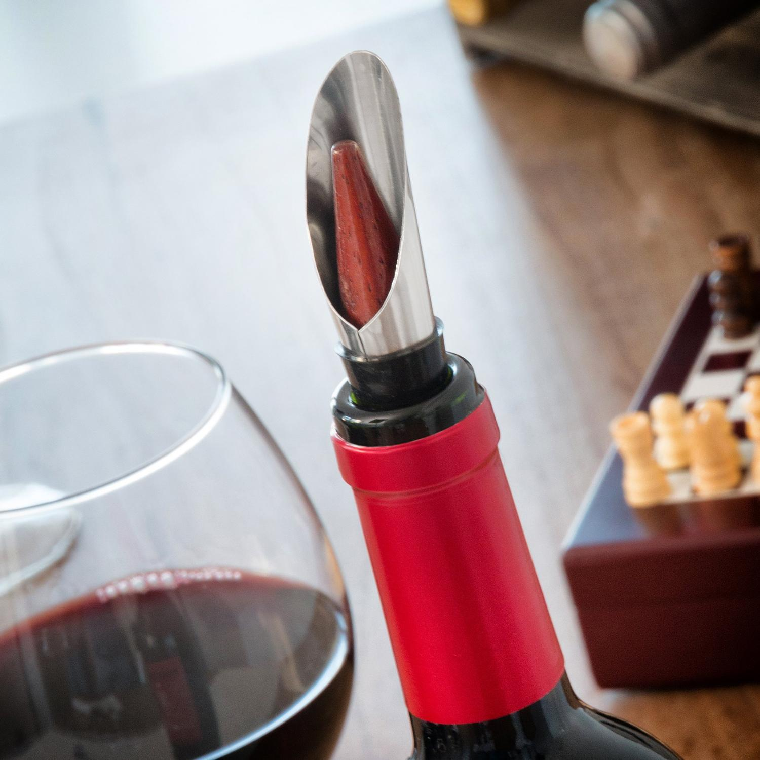 Botella de vino con vertedor, copa y juego de ajedrez.