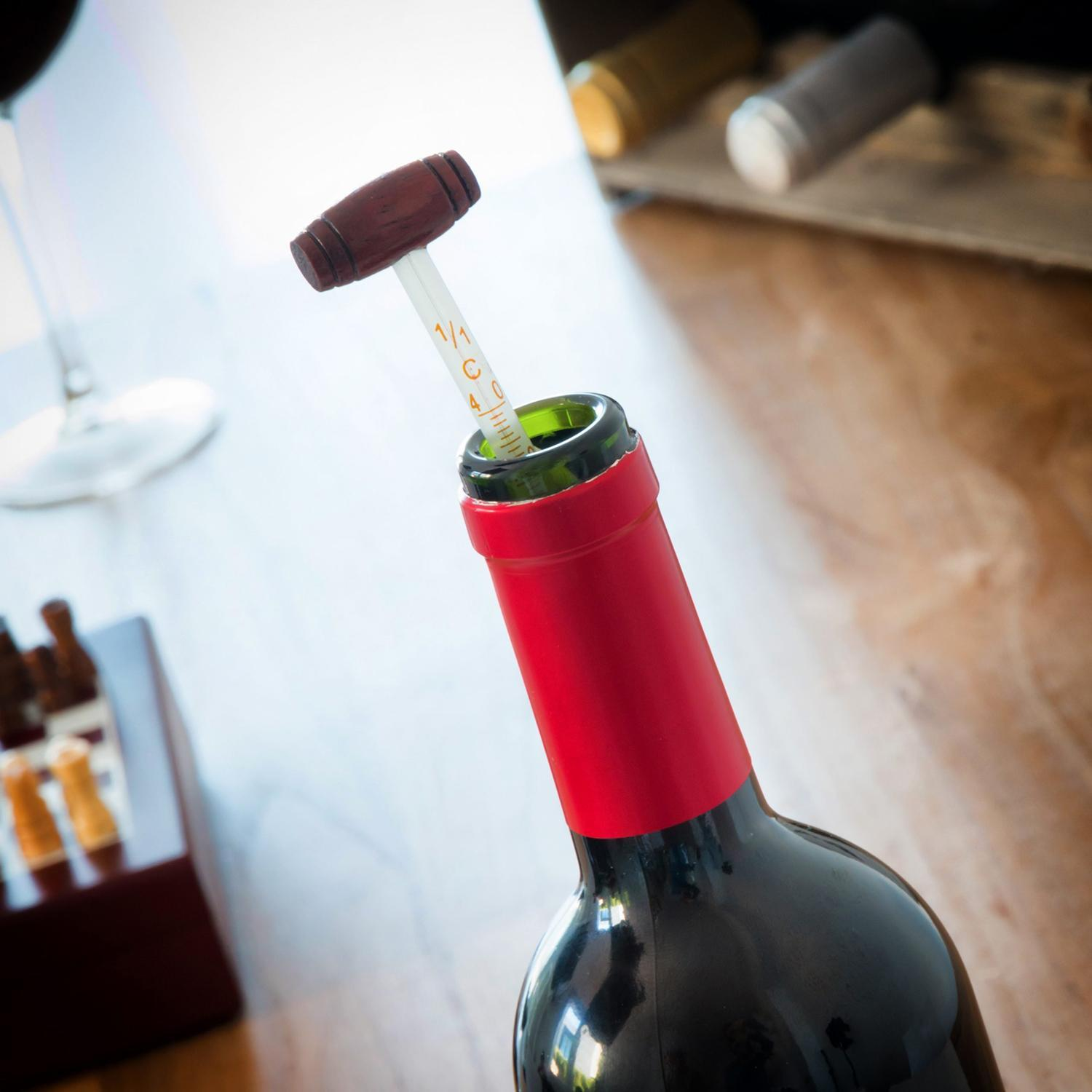 Una botella de vino con una herramienta de medición insertada. La herramienta está en la botella. La herramienta tiene un mango de madera.
