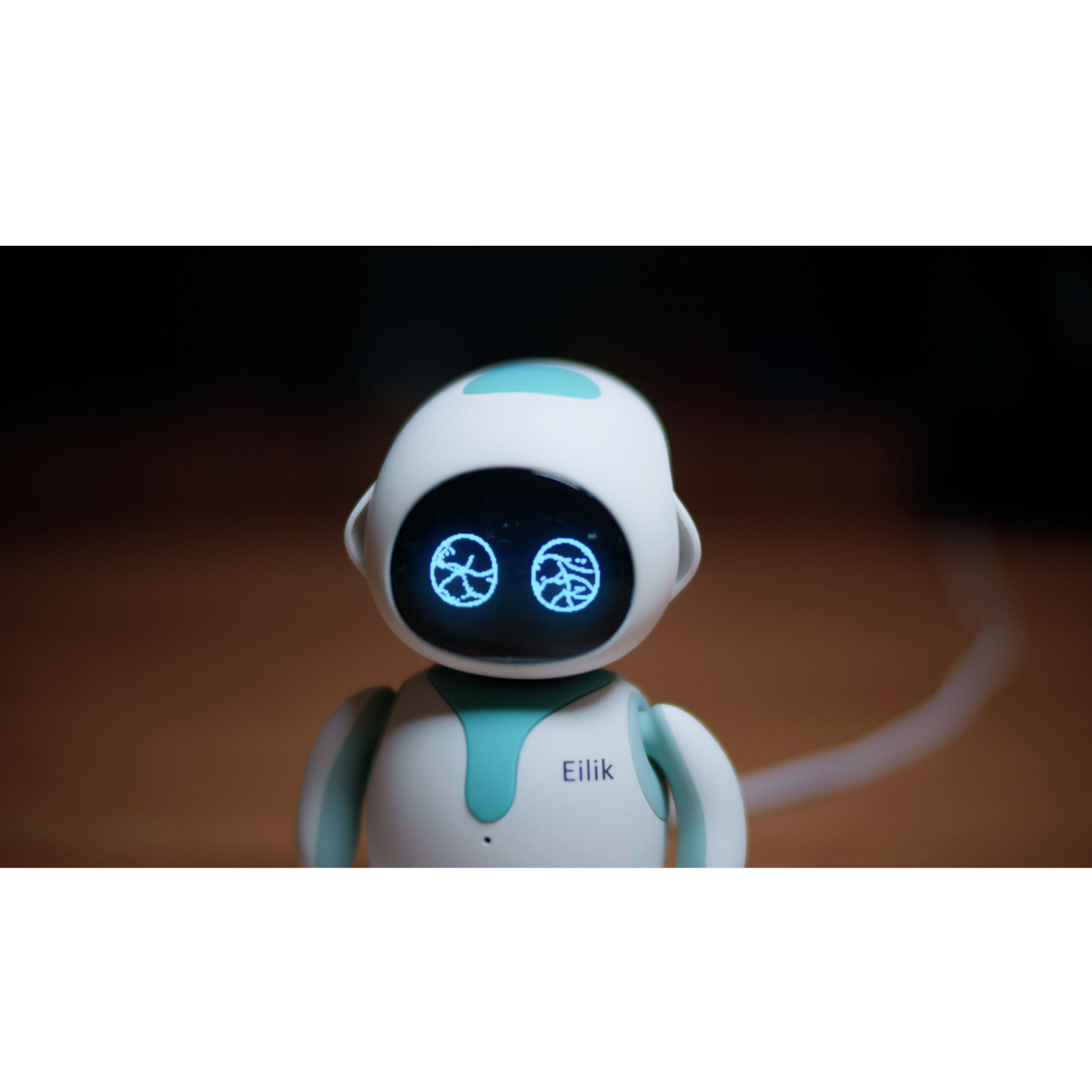 Ein weißer Roboter mit türkisfarbenen Akzenten, zwei leuchtenden blauen Augen. Der Roboter hat den Namen 'Eilik' auf der Brust.