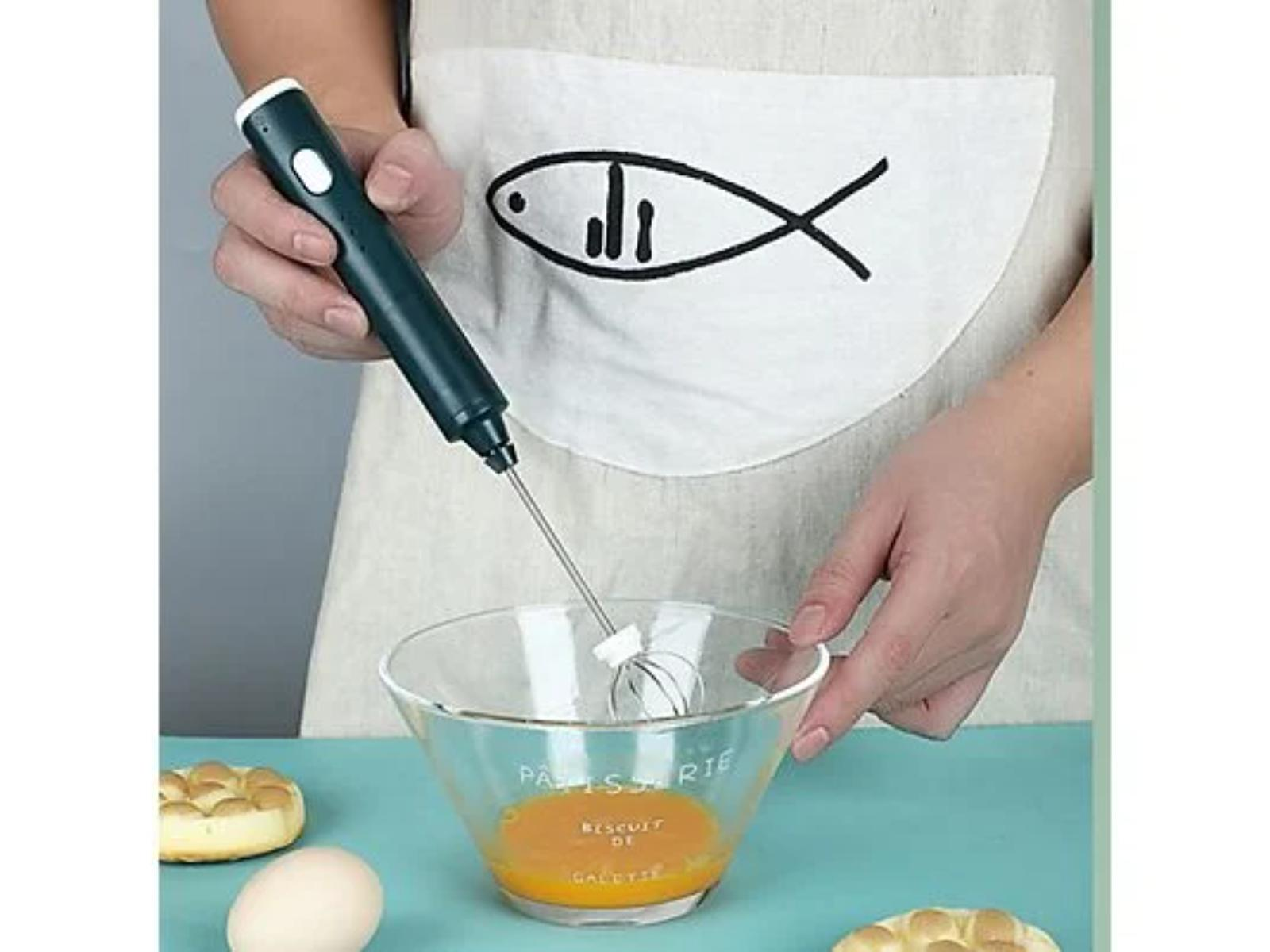 Hand hält einen Handmixer, verrührt Eigelb in einer Glasschüssel mit einem Schneebesen.