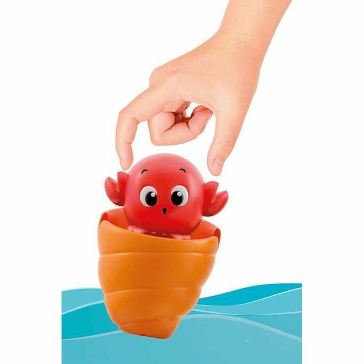 Una mano sosteniendo un cangrejo de juguete en una concha naranja, agua en el fondo. El juguete es rojo con ojos grandes.