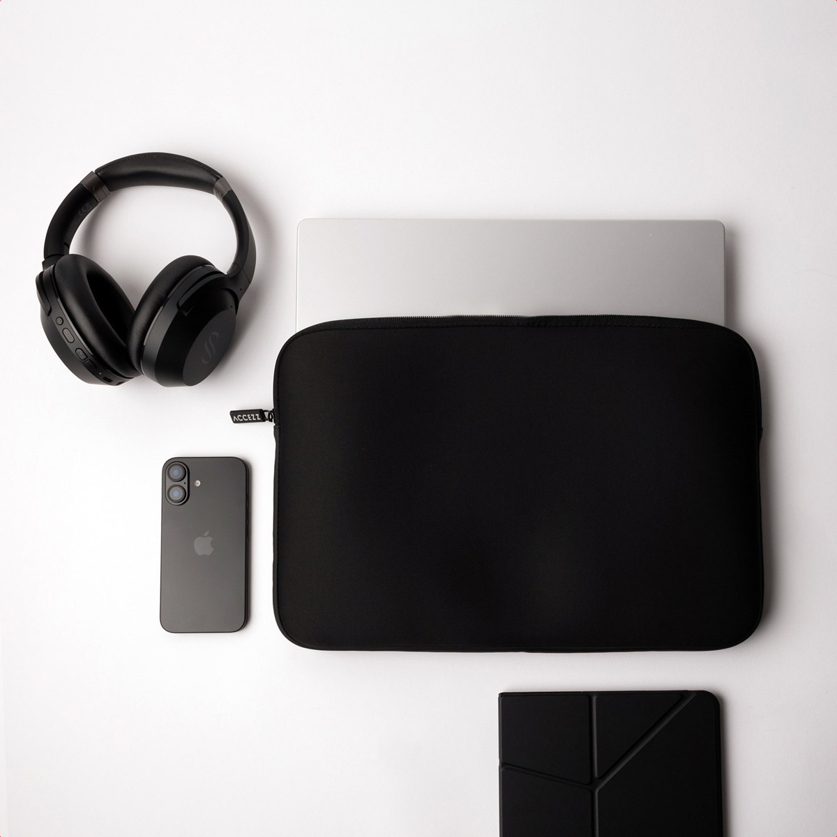 Black headphones, phone, laptop, case, and pad on a white surface.