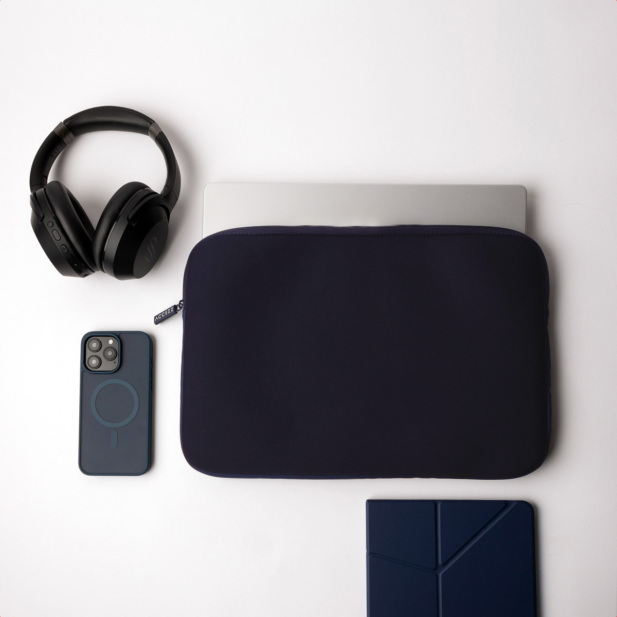 Top-down view of items: laptop, navy sleeve, phone, headphones, and tablet.