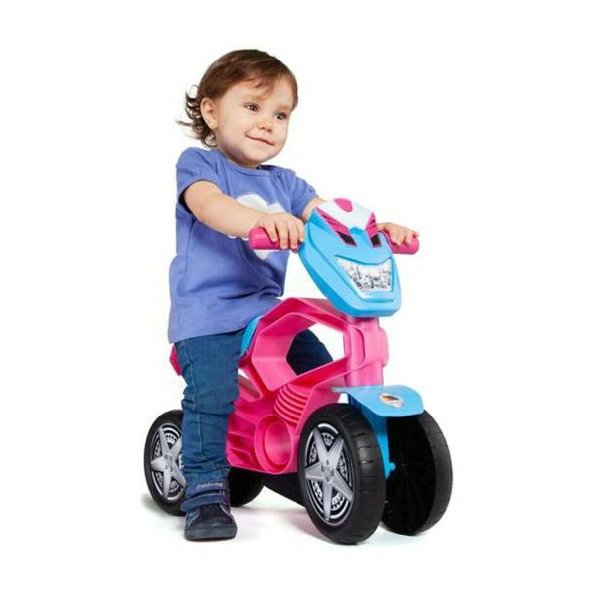 Un bambino piccolo è seduto su una moto giocattolo rosa e blu, sfondo bianco.