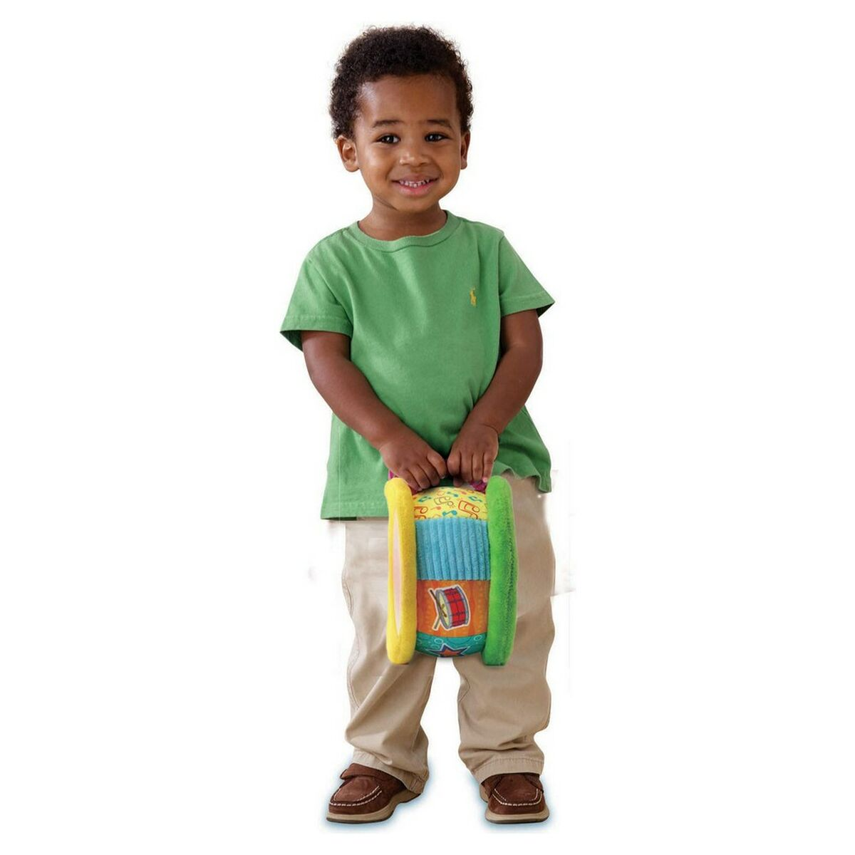 Un niño pequeño sosteniendo un tambor de juguete colorido. Sonríe, usa camisa verde y pantalones caqui.
