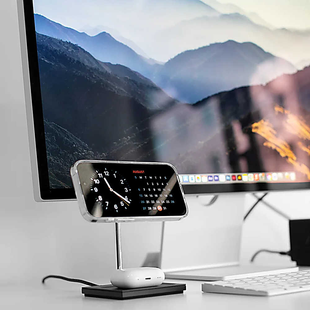 Telefono su supporto con calendario di agosto, accanto a monitor con vista montagna.