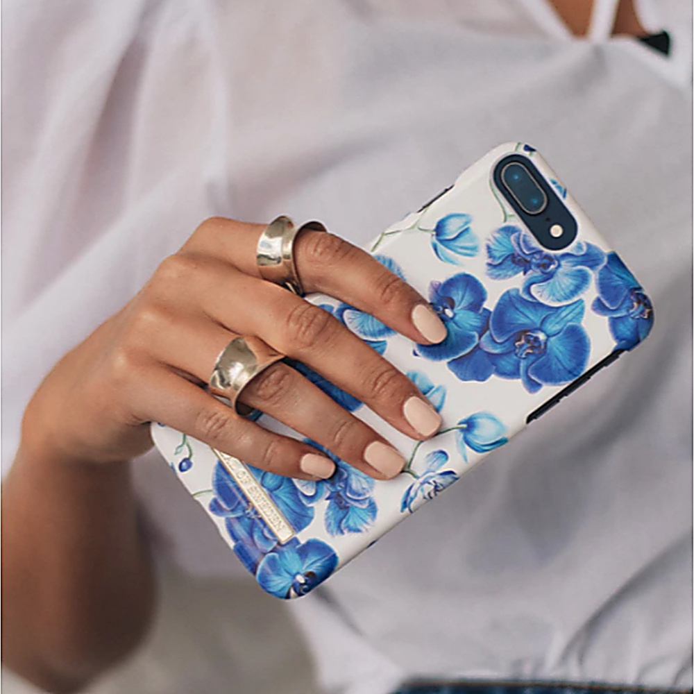 Donna che tiene una custodia per telefono con un design floreale blu. Indossa anelli e ha unghie lunghe.
