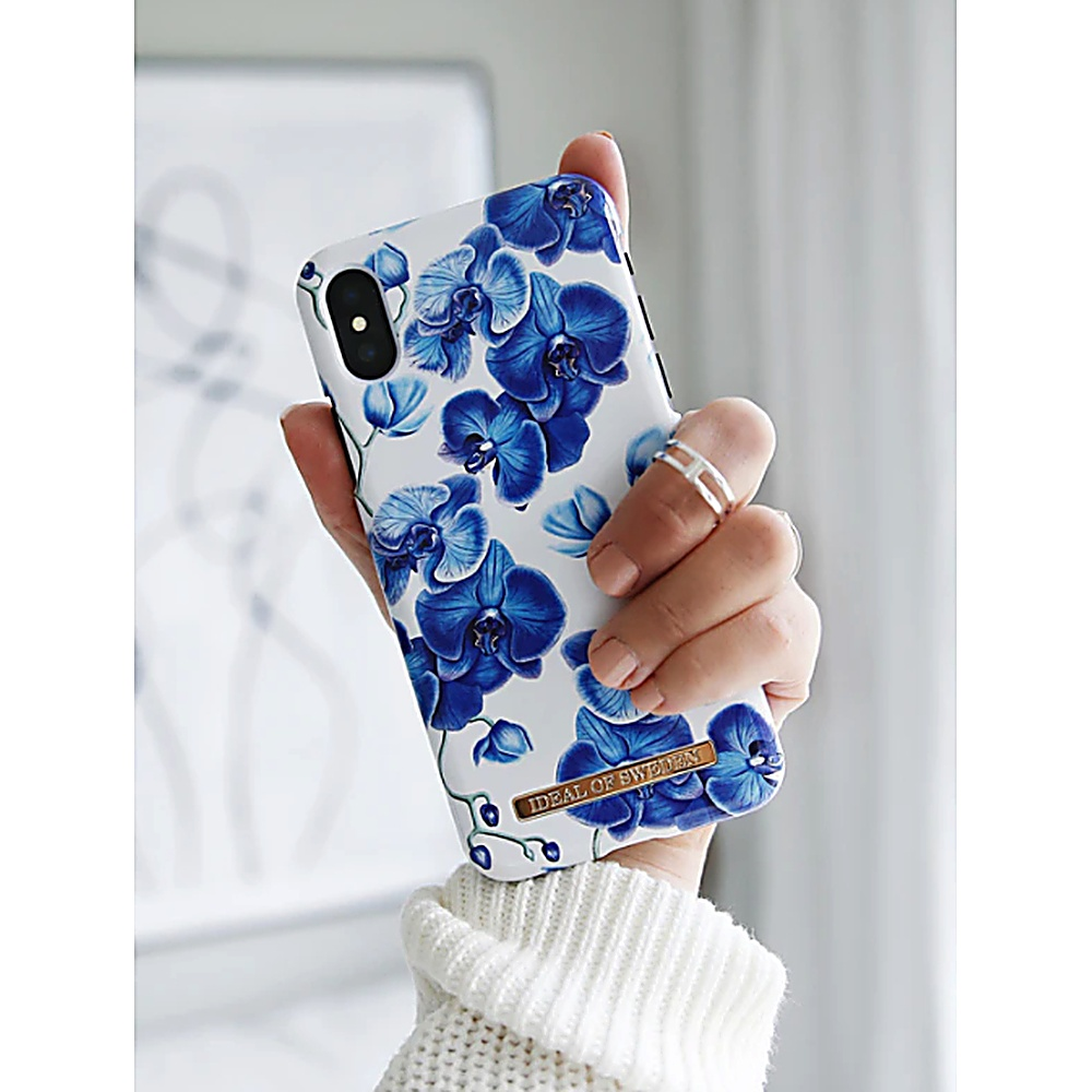 Mano che tiene una custodia per telefono con un design floreale blu. La custodia ha uno sfondo bianco.