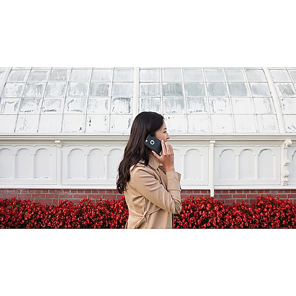 Donna che parla al telefono, fuori da un edificio bianco con fiori rossi.