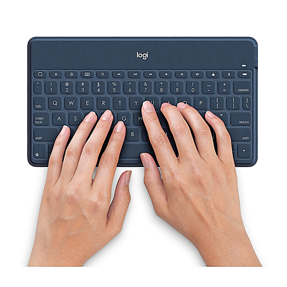 Le mani di una persona che digitano su una tastiera blu scuro. La tastiera è su una superficie bianca.