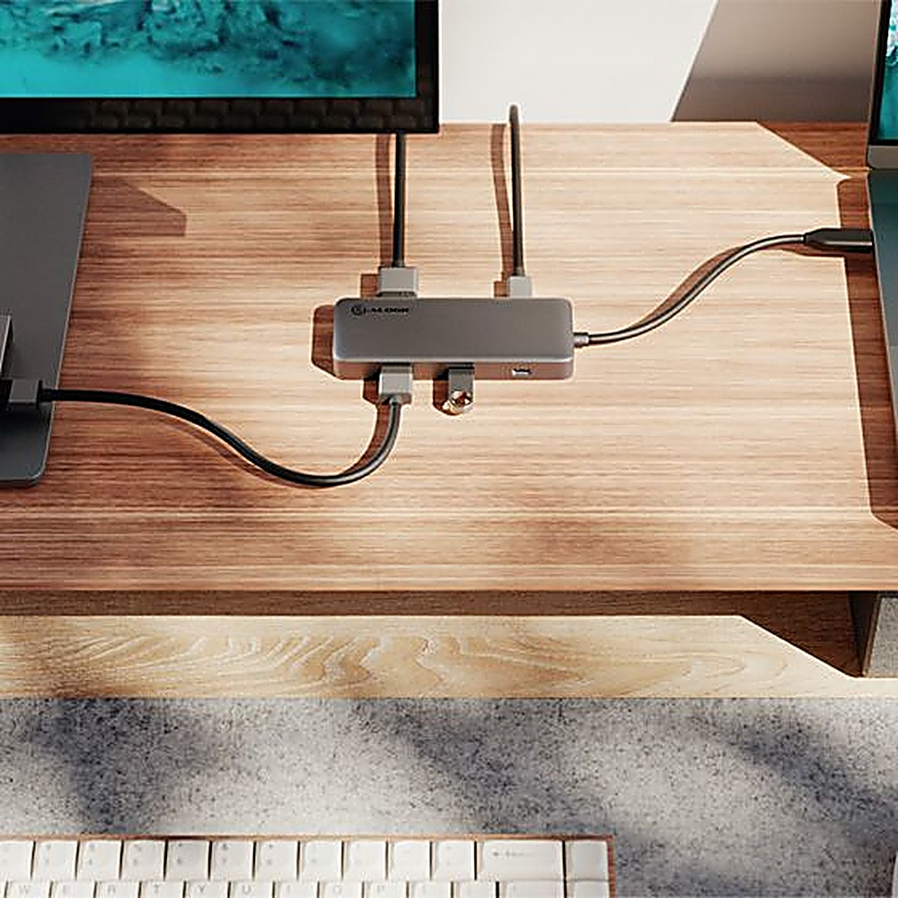 Una scrivania in legno con un hub, un laptop e un monitor. I cavi collegano tutto.