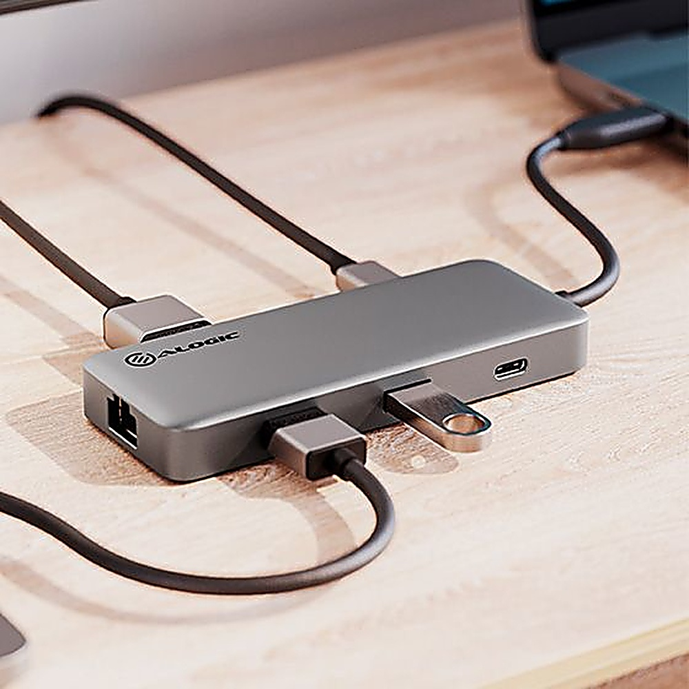 Un hub USB-C ALOGIC grigio collegato a più dispositivi su una scrivania di legno.