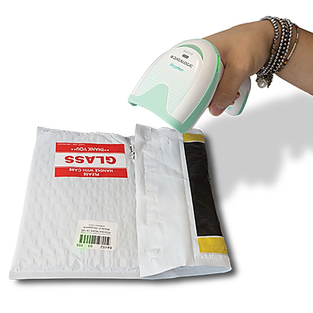 Una mano tiene un lettore di codici a barre verde menta sopra un pacco con l'etichetta 'GLASS'. Il pacco è bianco e imbottito.