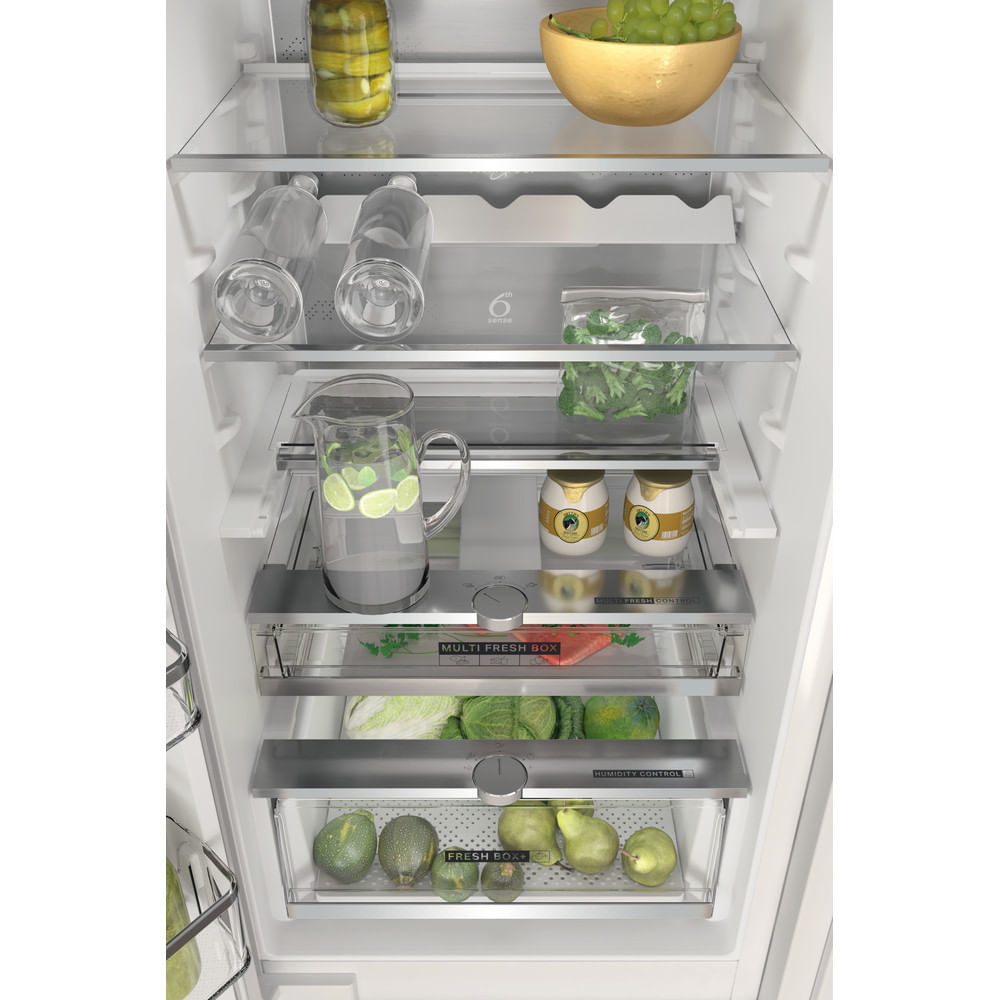 Interno di frigorifero aperto. Barattoli, bottiglie, brocca con limoni e prodotti freschi visibili.