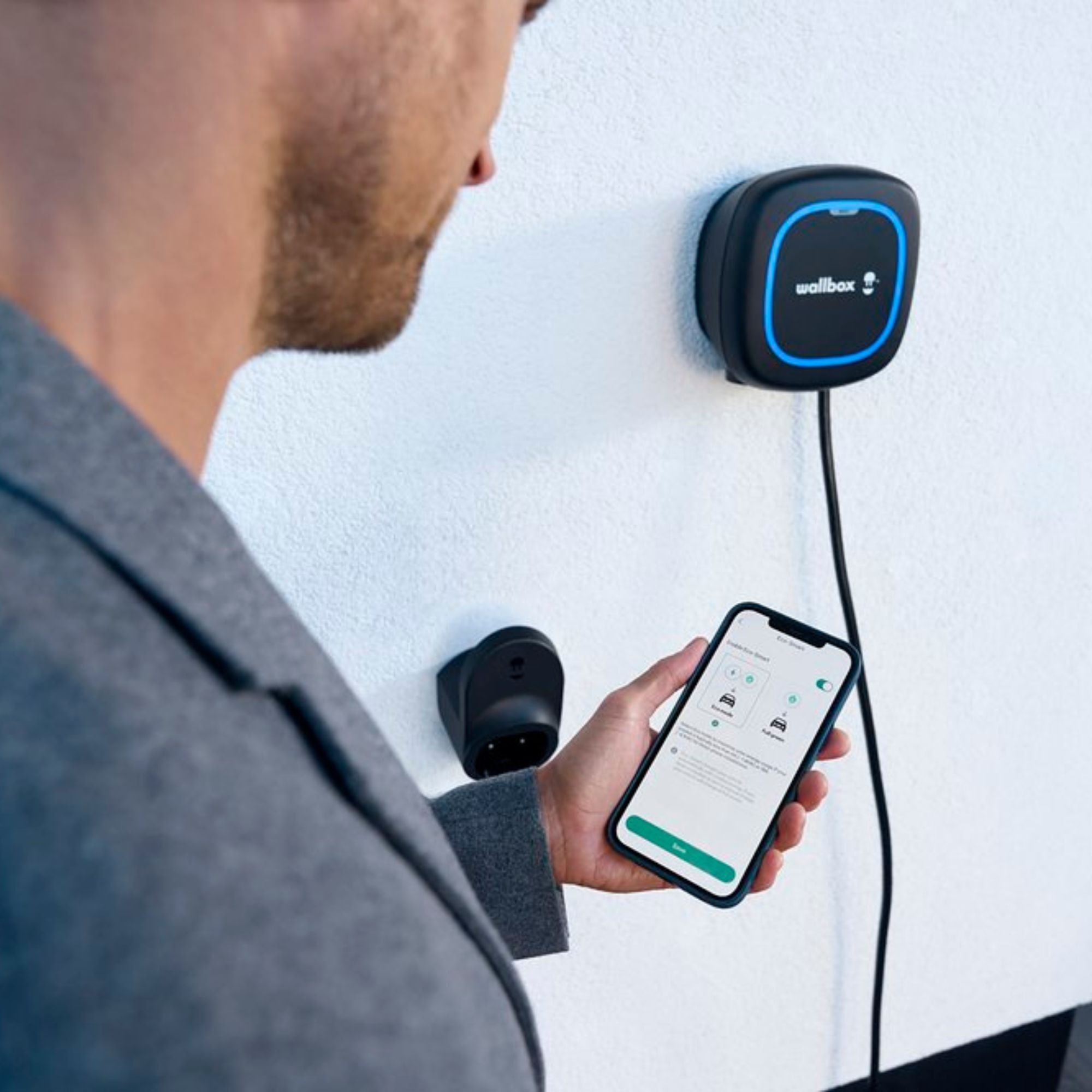 Mann mit Telefon in der Nähe eines Wandladegeräts. Ein schwarzes Ladegerät ist an einer Wand montiert.