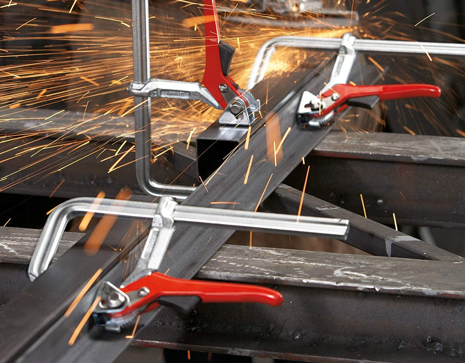 Metallbearbeitungsszene mit Funkenflug. Drei rotgriffige Klemmen.