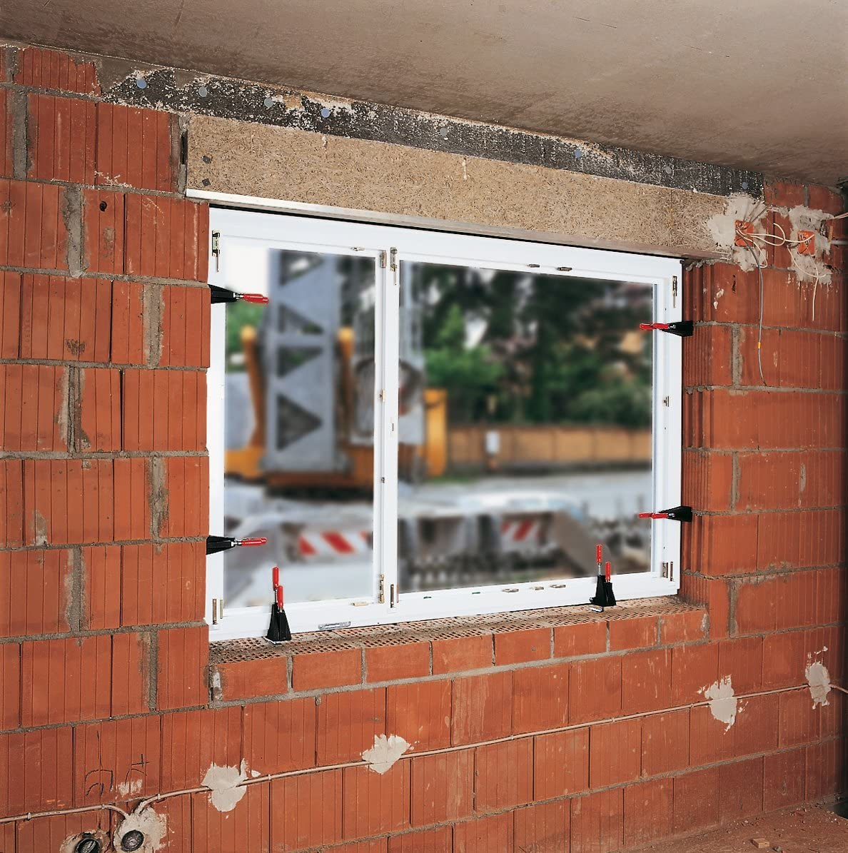 In eine Ziegelmauer eingespannter Fensterrahmen. Baustellenszene mit sichtbaren Baumaterialien.