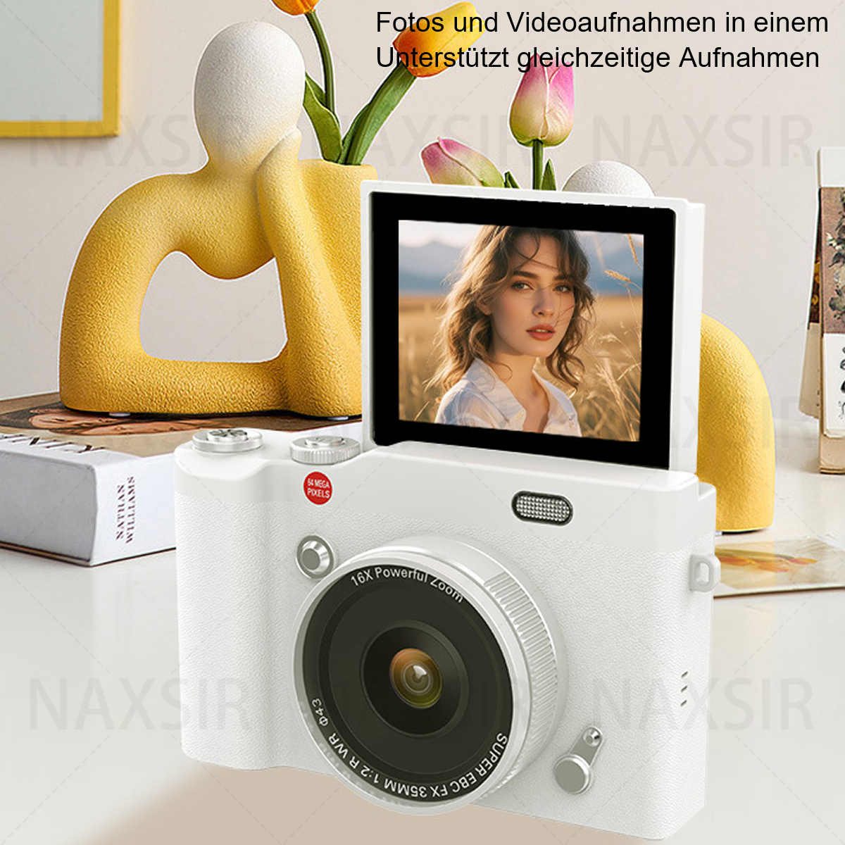 Fotocamera bianca con schermo che mostra il ritratto di una donna, posizionata su un tavolo con fiori e libri.