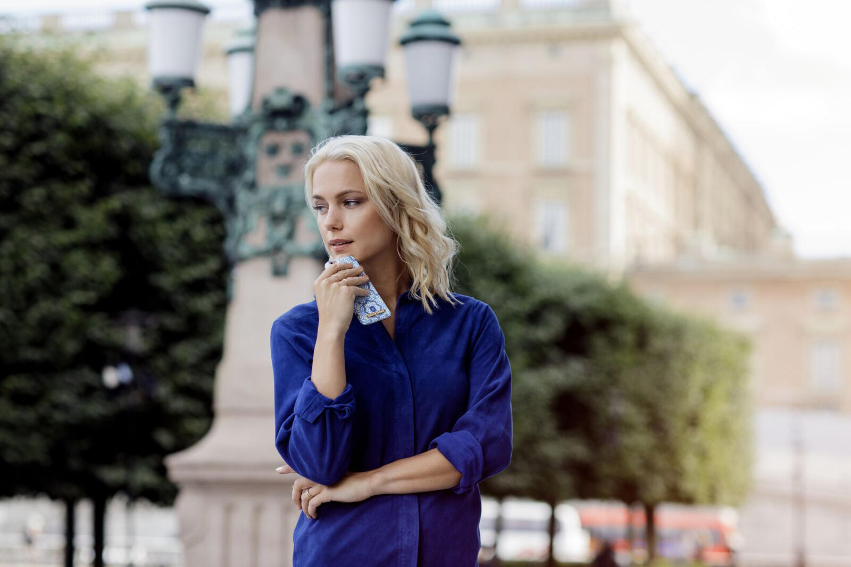 Donna bionda con camicia blu tiene custodia con design blu e bianco, all'aperto.