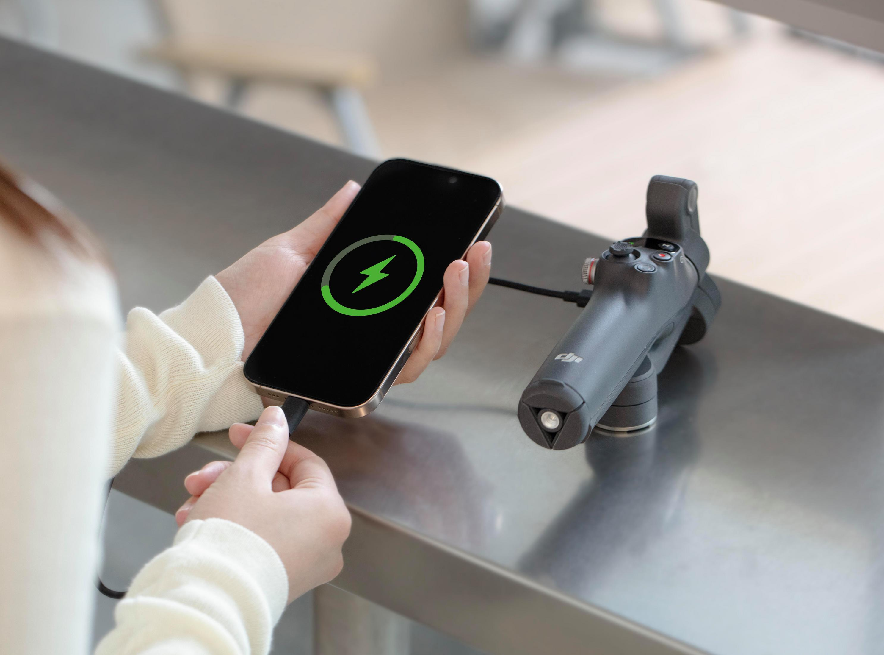 Osoba ładująca telefon z zieloną ikoną błyskawicy, używając stabilizatora gimbala.