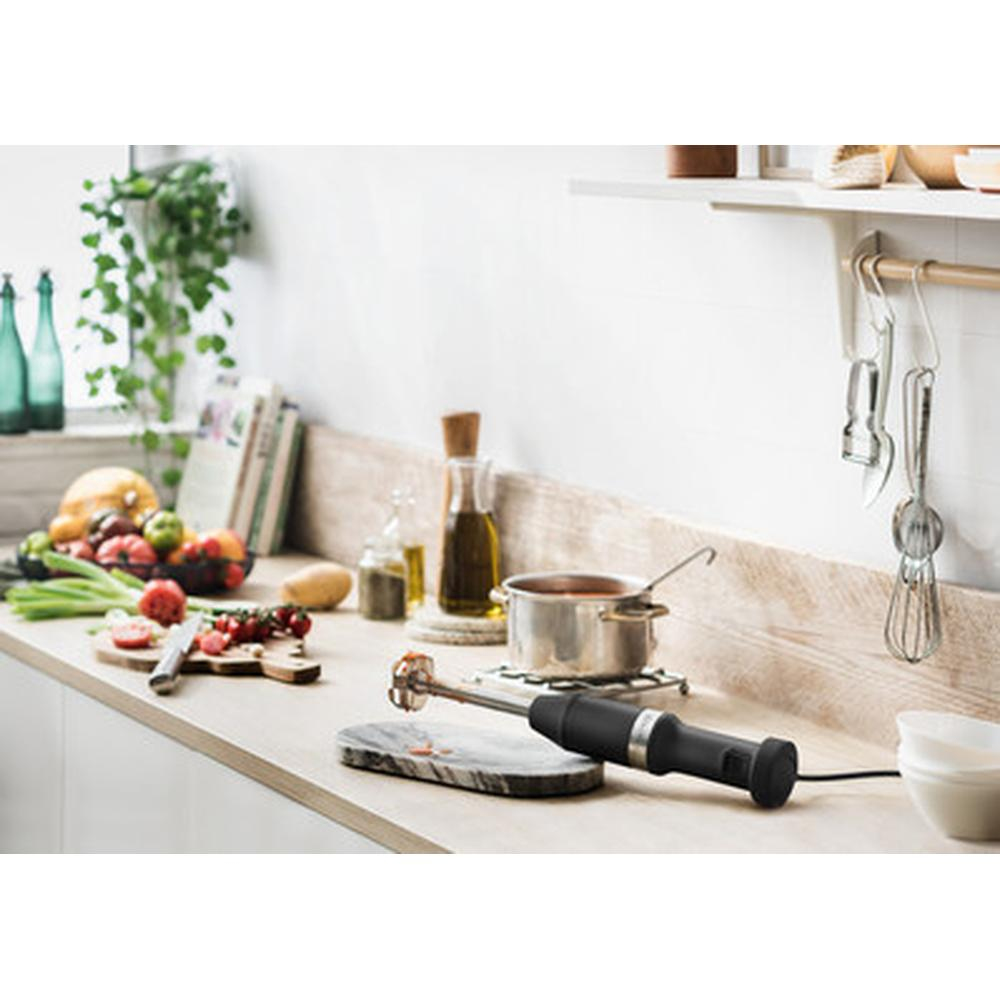 A kitchen counter with food and a black hand blender in use.