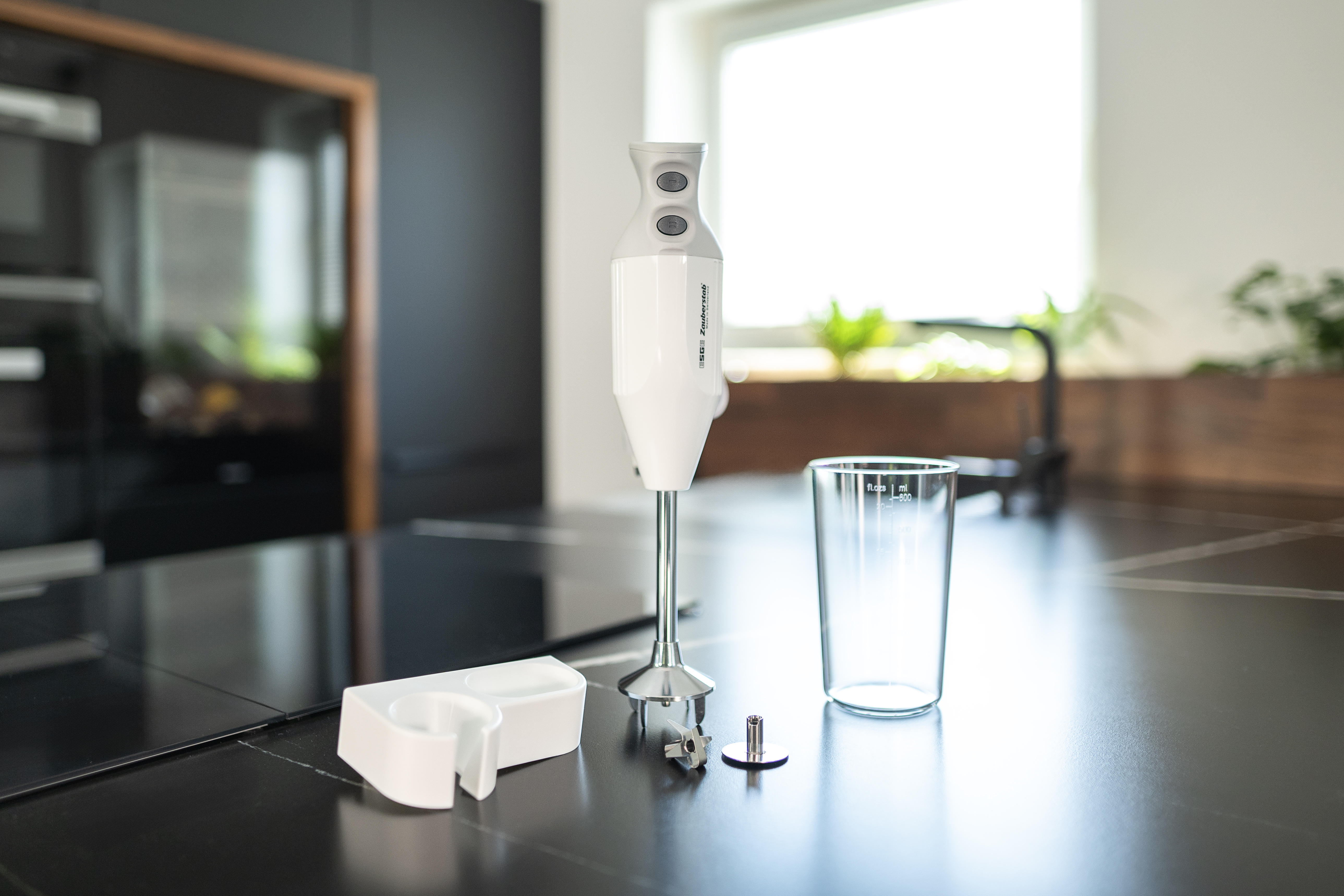 Cucina con un frullatore e accessori su un ripiano. Sono presenti un bicchiere e un supporto bianco.