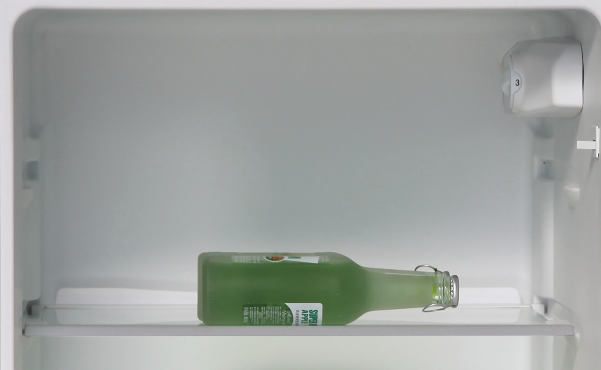 Bottiglia di liquido verde all'interno di un frigorifero bianco. Ripiani e pareti bianche.
