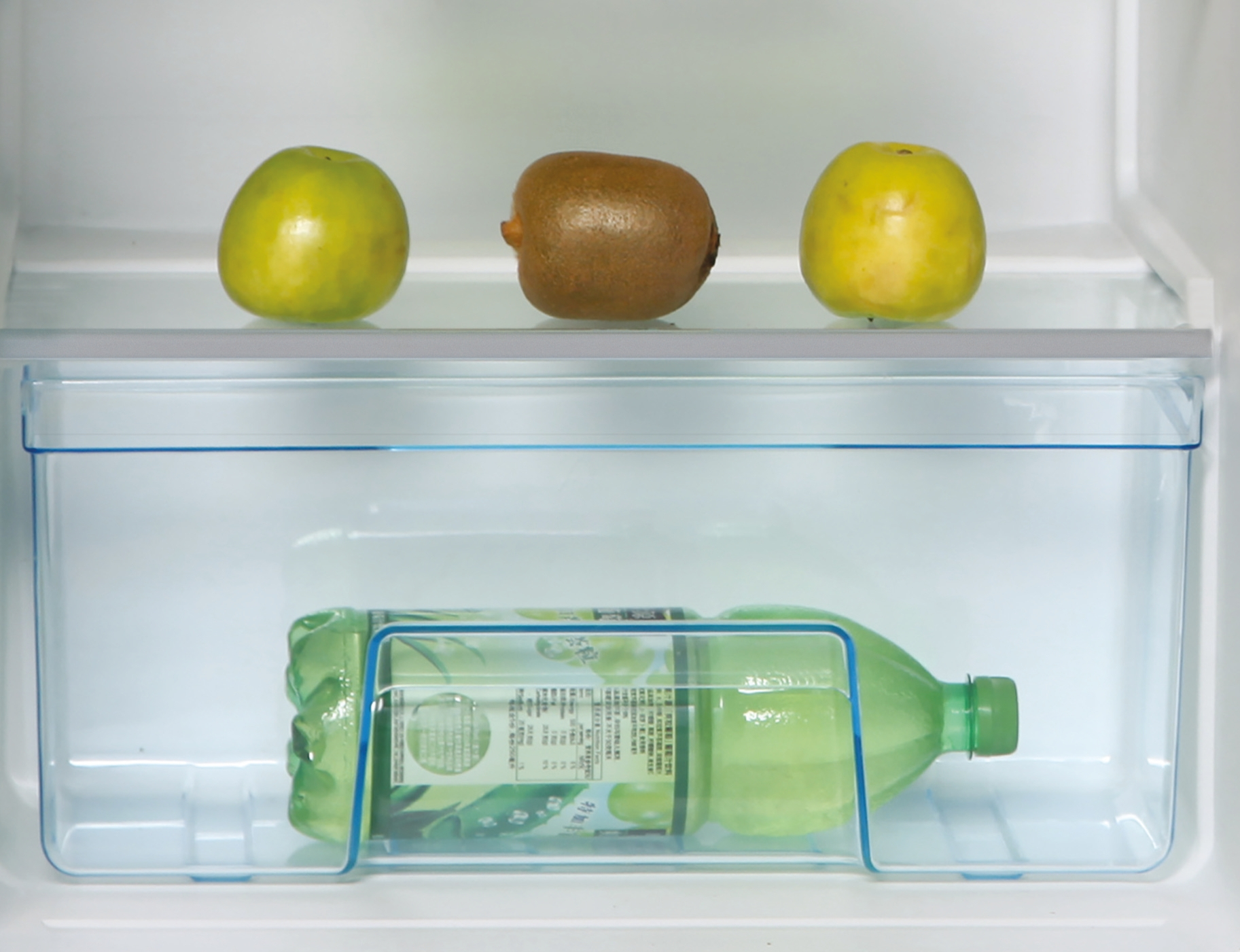 Tre frutti e una bottiglia di succo all'interno di un frigorifero.