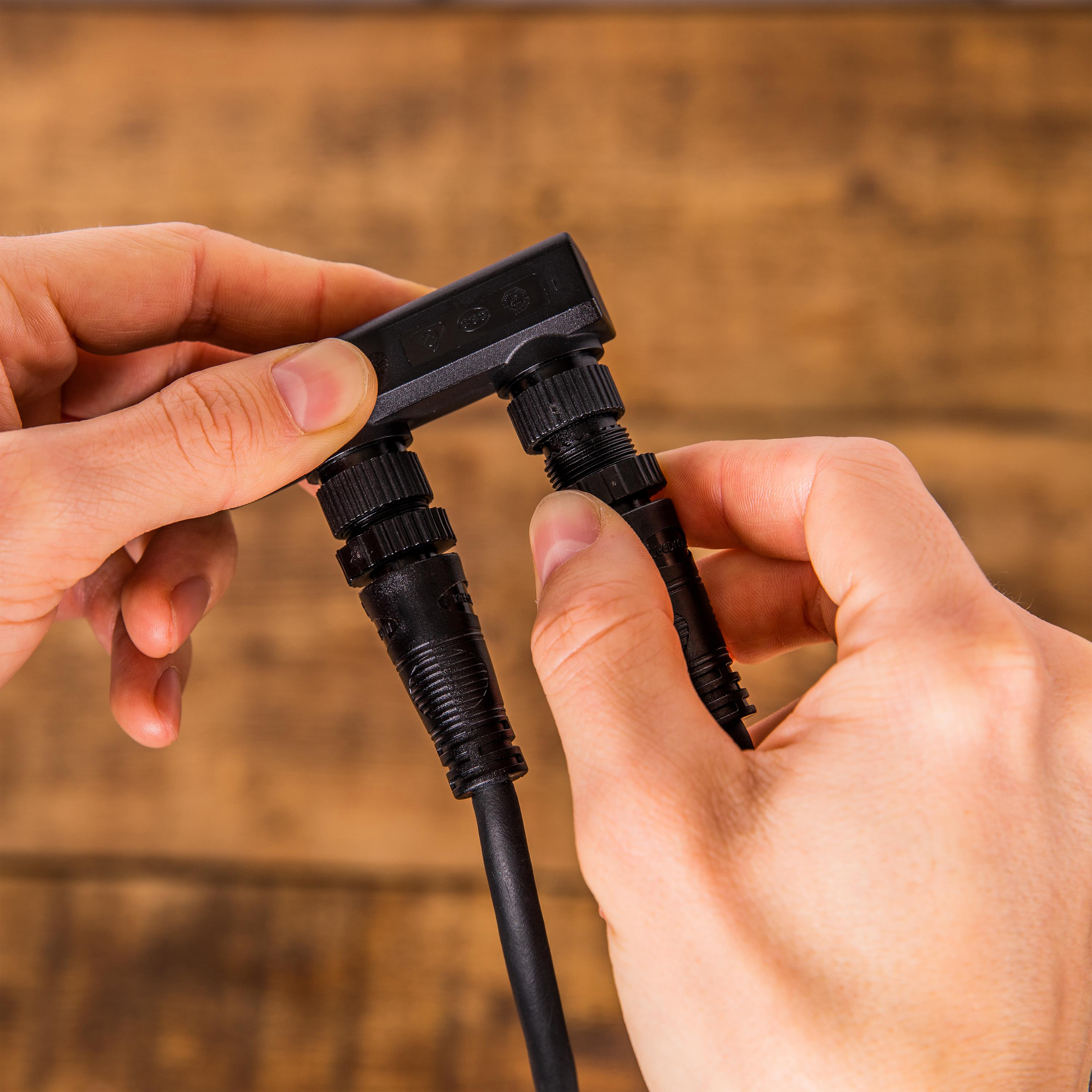 Hände verbinden zwei schwarze elektrische Stecker, einer L-förmig, auf Holzgrund.