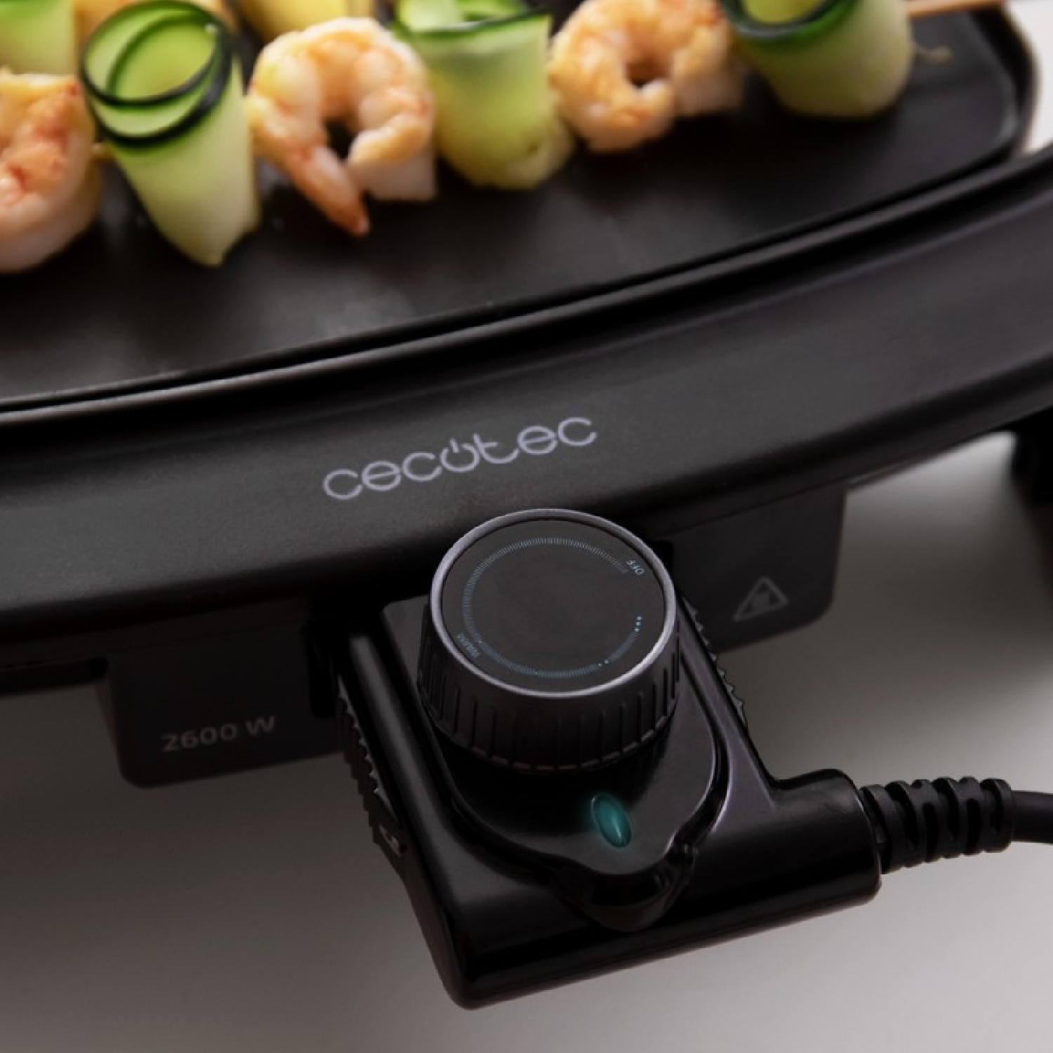Parrilla negra con brochetas de camarones y pepinos. Un panel de control con dial está enfocado.
