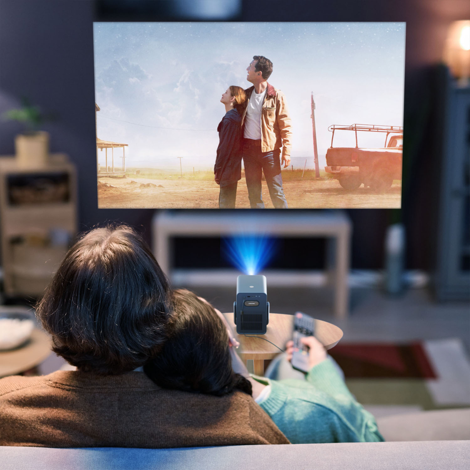 Deux personnes regardent un film projeté sur un mur. Un petit projecteur est sur une table.