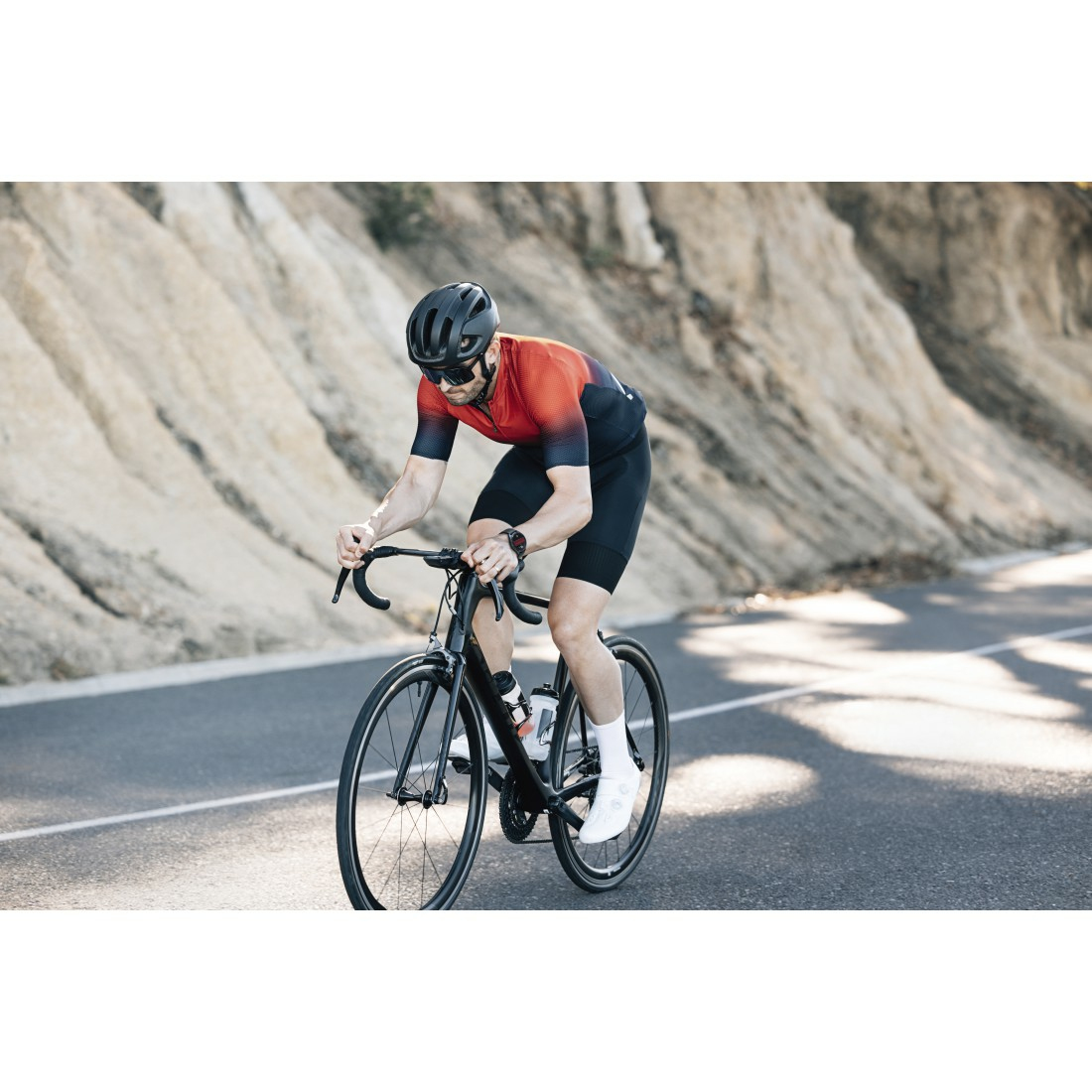 Un cycliste en tenue rouge et noire fait du vélo de route noir sur une route pavée. L'arrière-plan est flou.